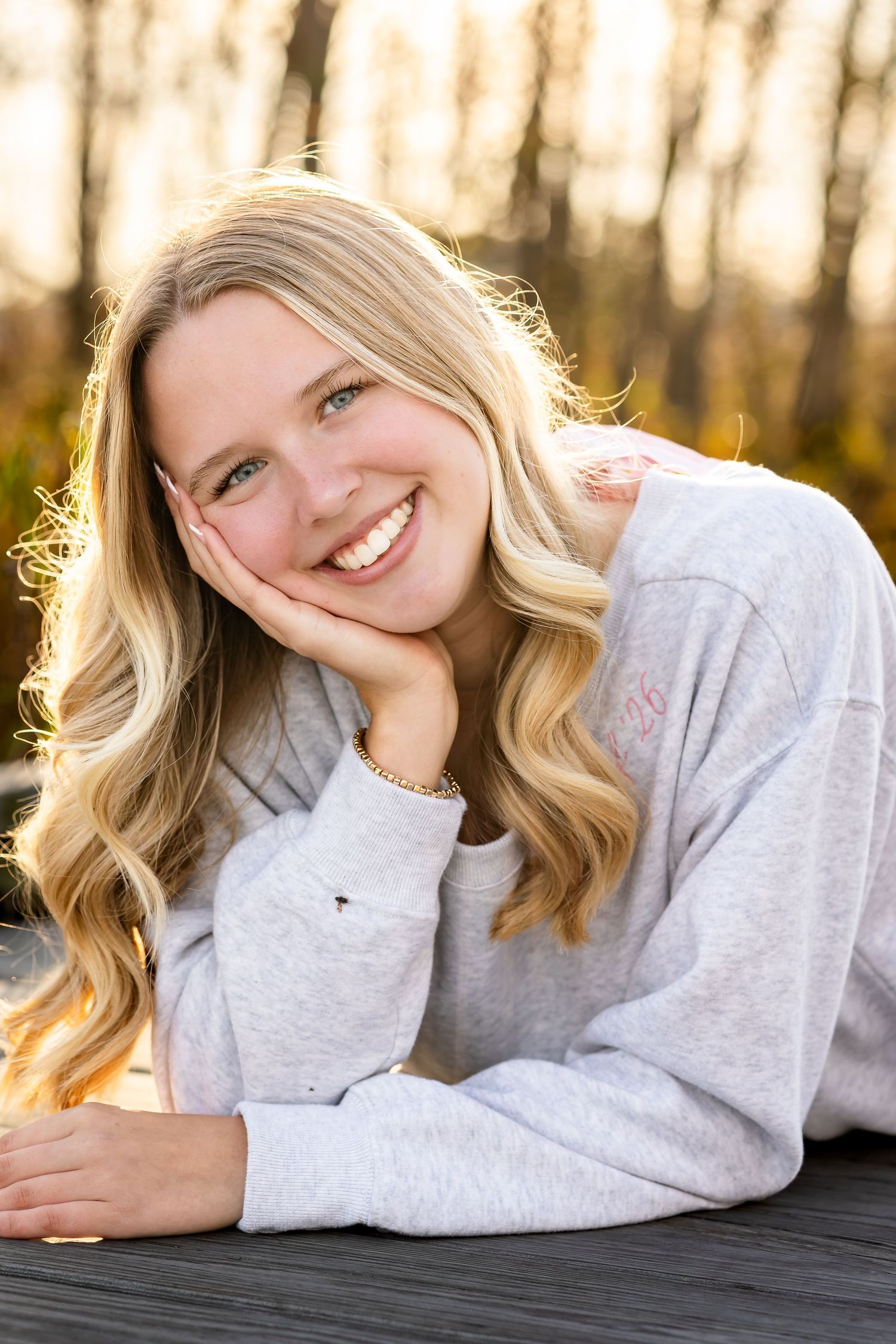 Relaxed portraits in a gray sweater with natural backlighting from sunset through trees.