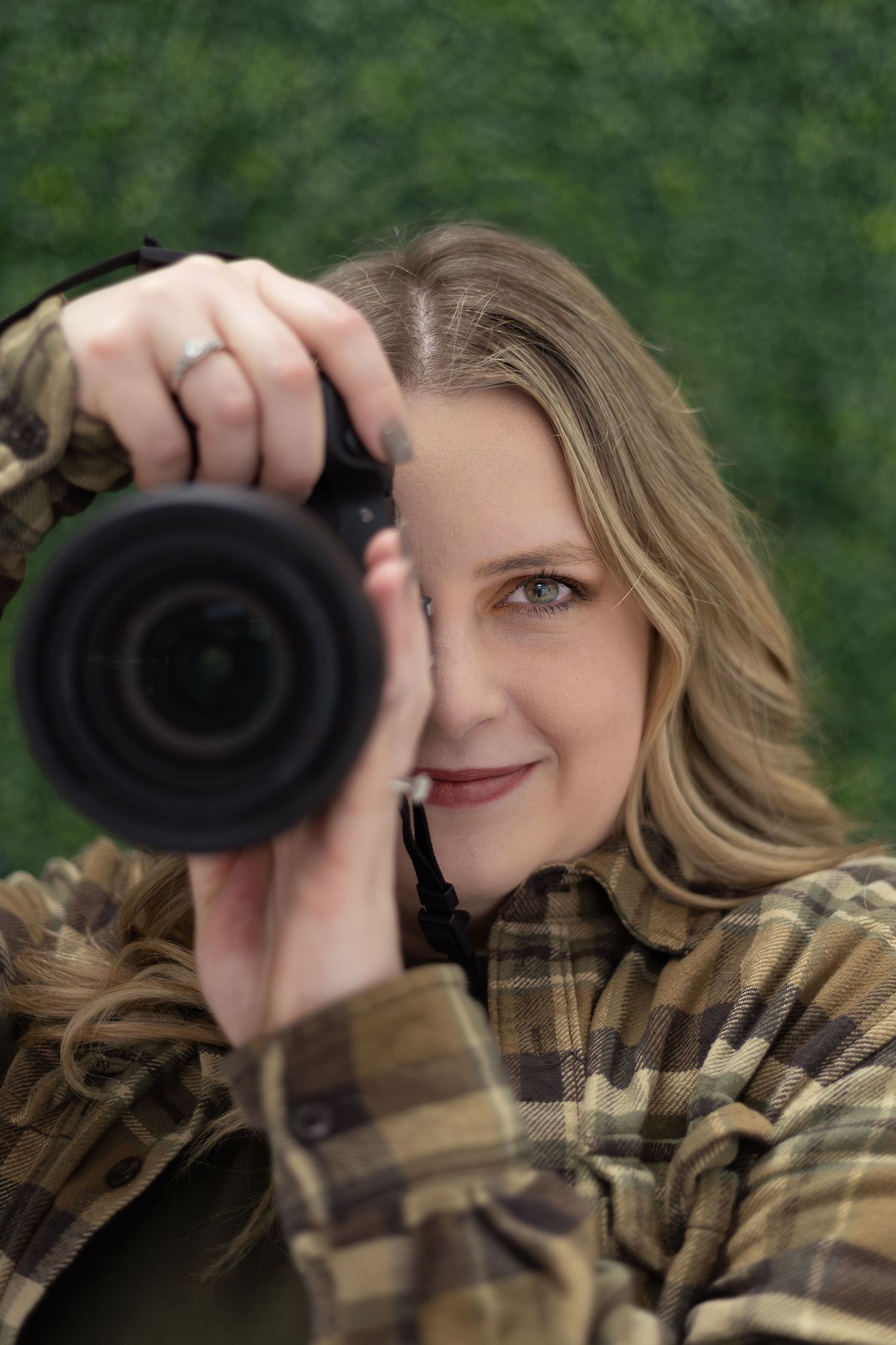 Person in plaid shirt using binoculars to observe wildlife in a green forest setting.