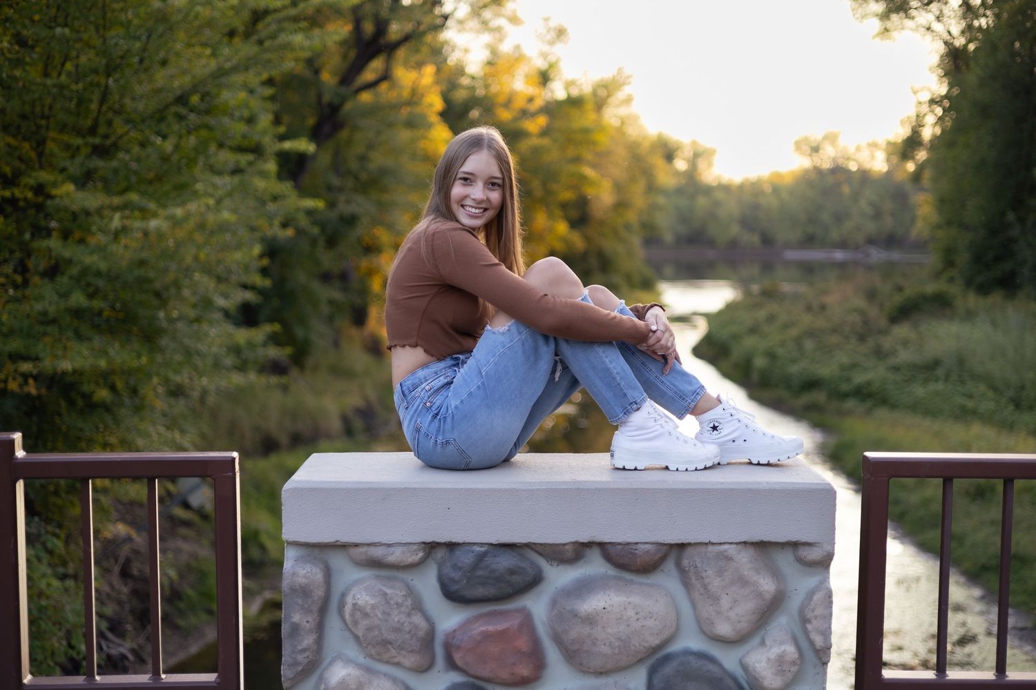 Person relaxing on stone wall during outdoor sunset photoshoot.