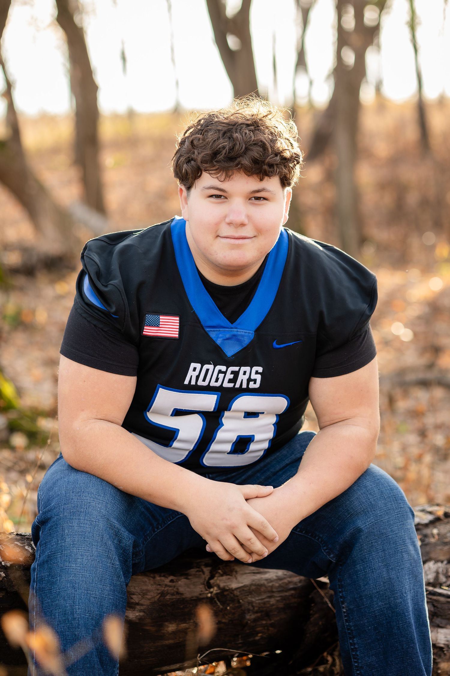 Person wearing Rogers football jersey sitting on fallen log in autumn forest.