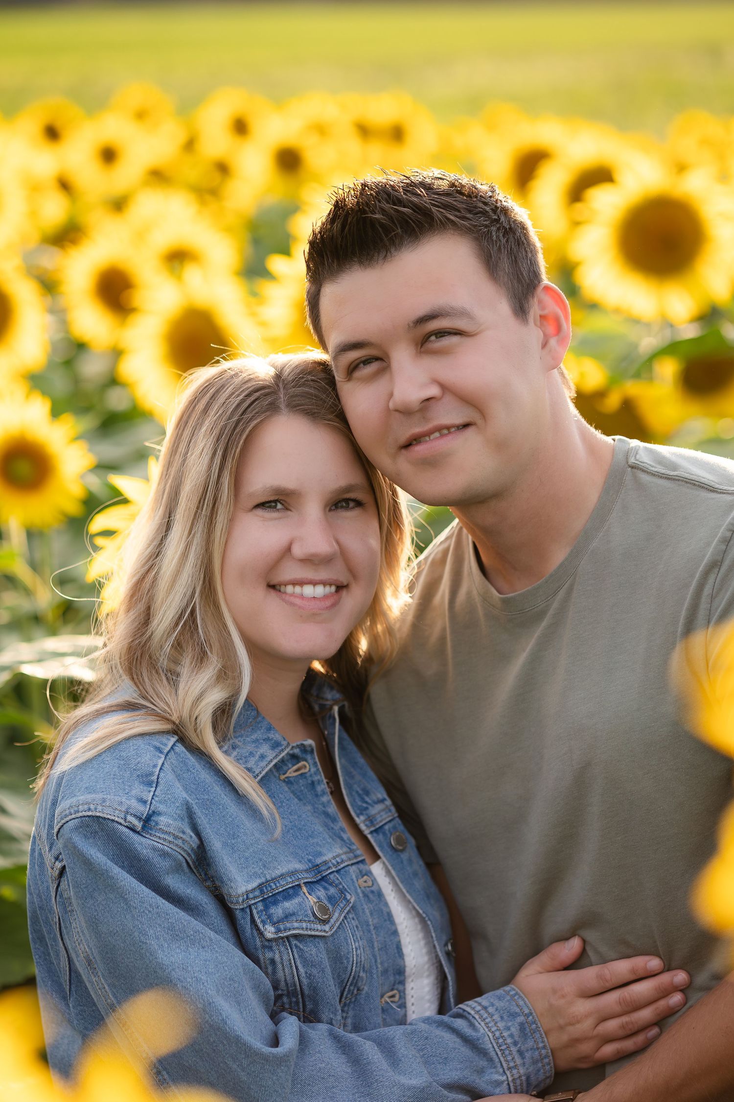 Couple poses together in vibrant sunflower field during golden hour.