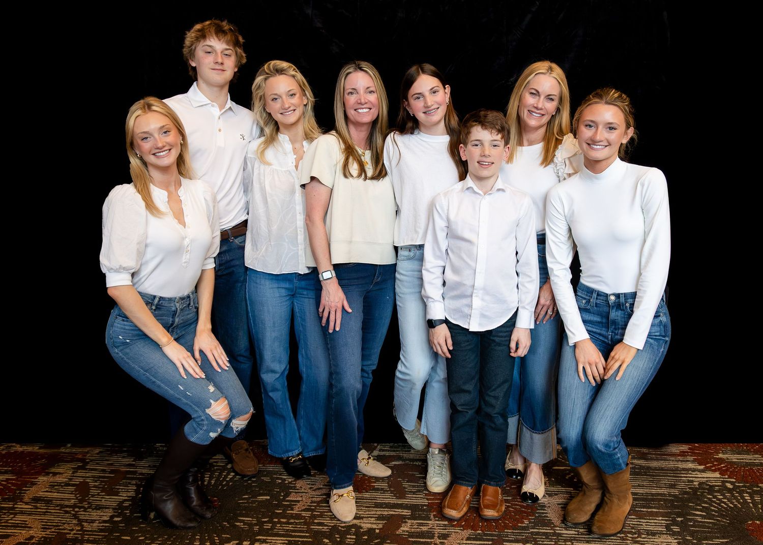 Group portrait showing matching outfits of white tops and blue jeans in casual studio setting.