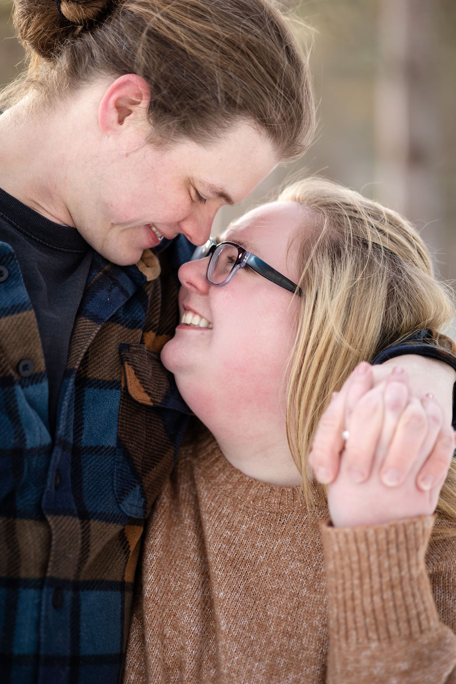 A young couple shares a tender forehead-to-forehead moment, smiling closely together outdoors in warm casual attire.