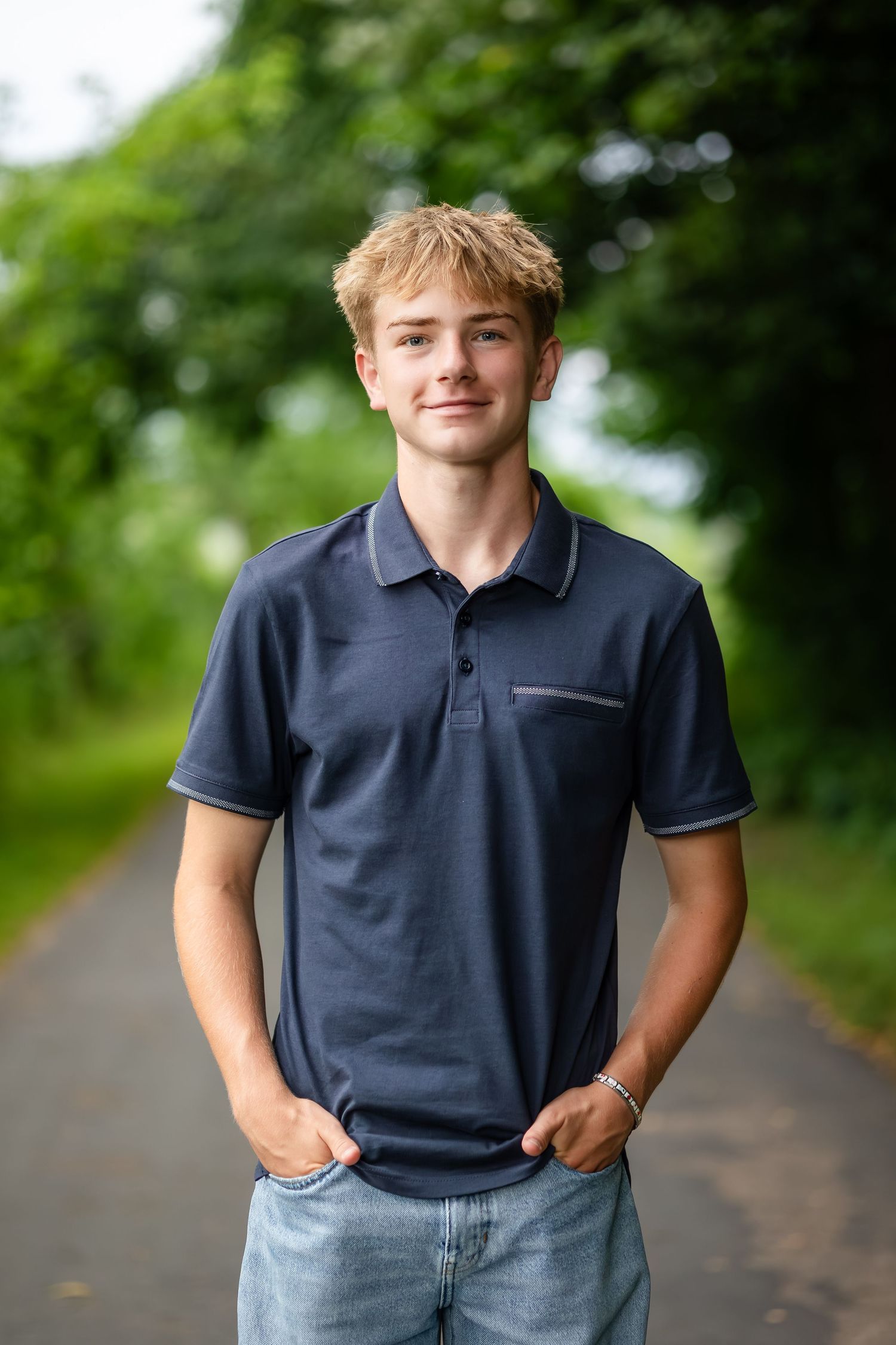 Person in navy polo shirt poses casually on tree-lined path.