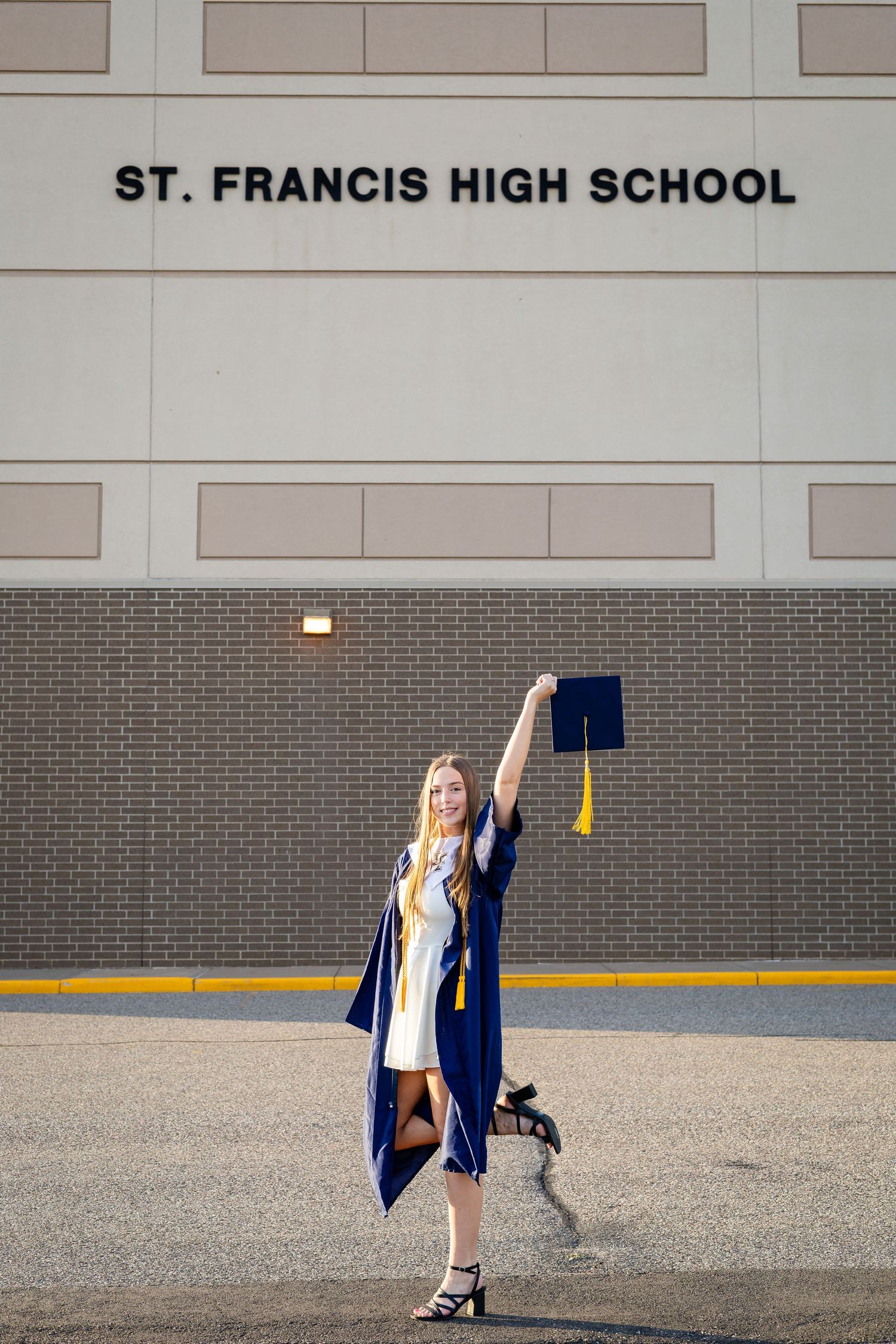 Graduate in cap and gown poses in front of St. Francis High School building sign.