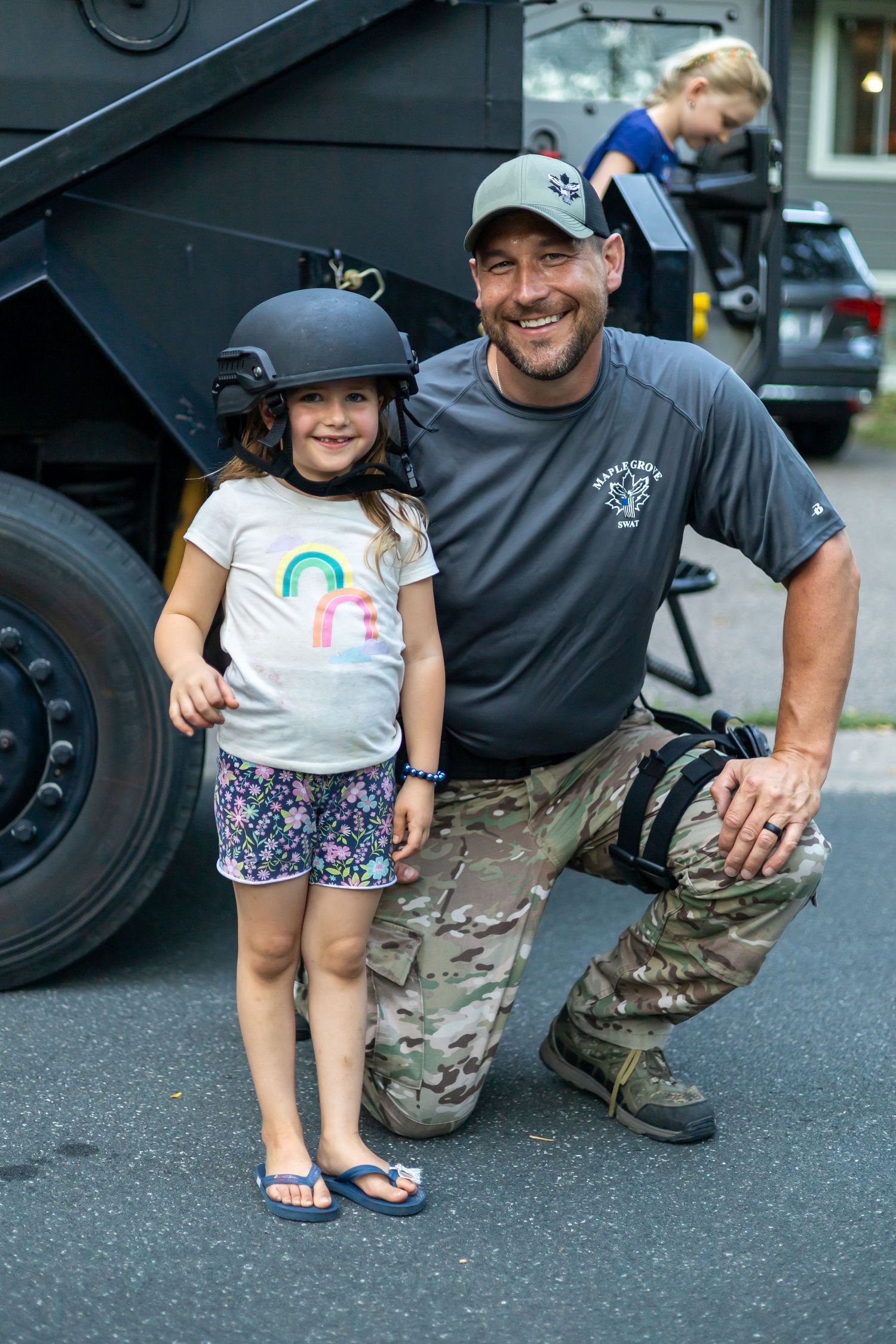 SWAT team members in tactical gear interacting with a child near an armored vehicle.