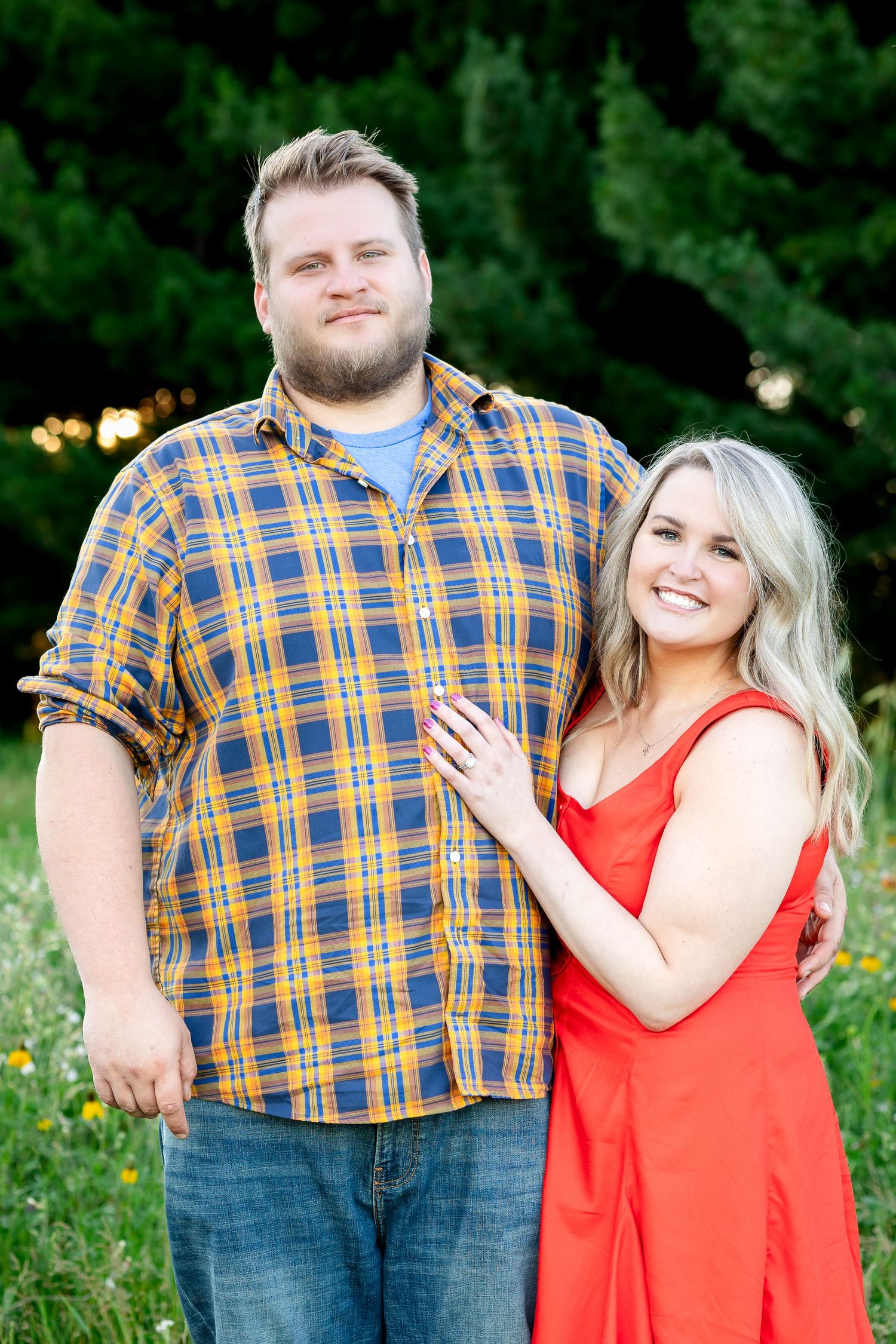 Couple in casual attire posing together in a green summer meadow.