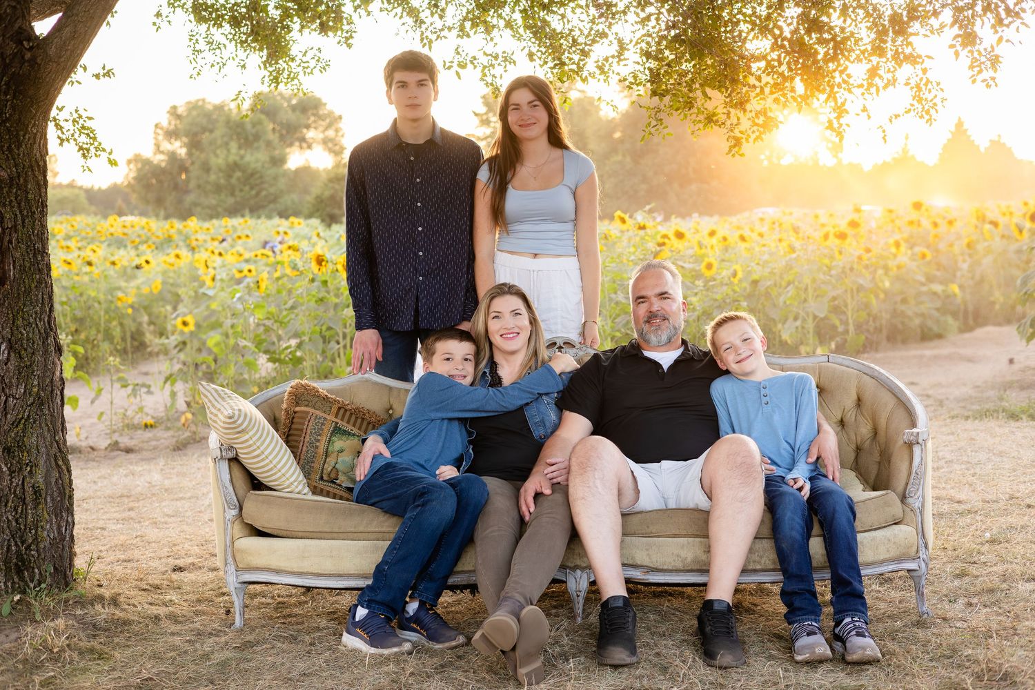 Family members sit together on a rustic bench during sunset with golden light filtering through trees.