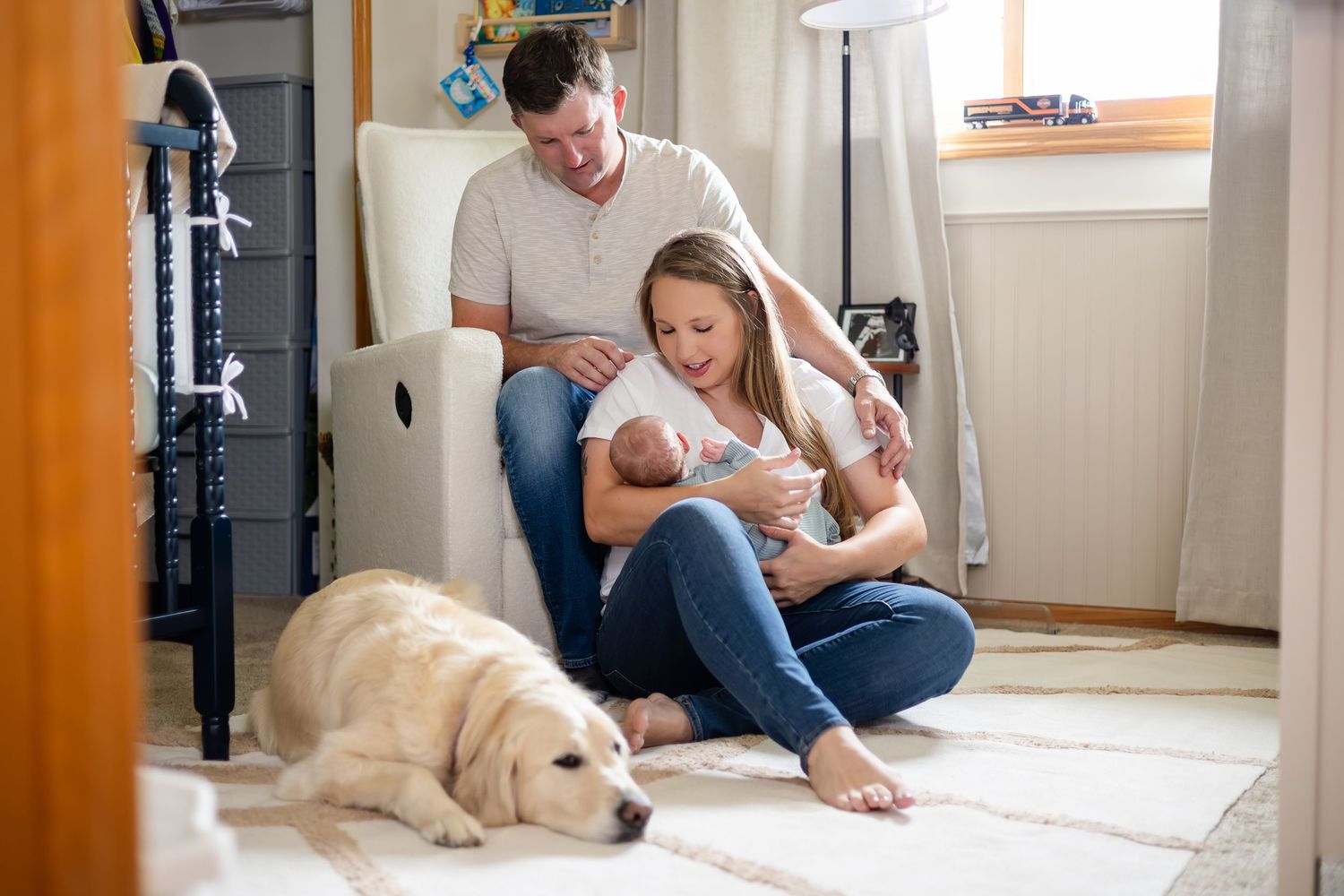 Intimate family moment in nursery with golden retriever resting nearby.