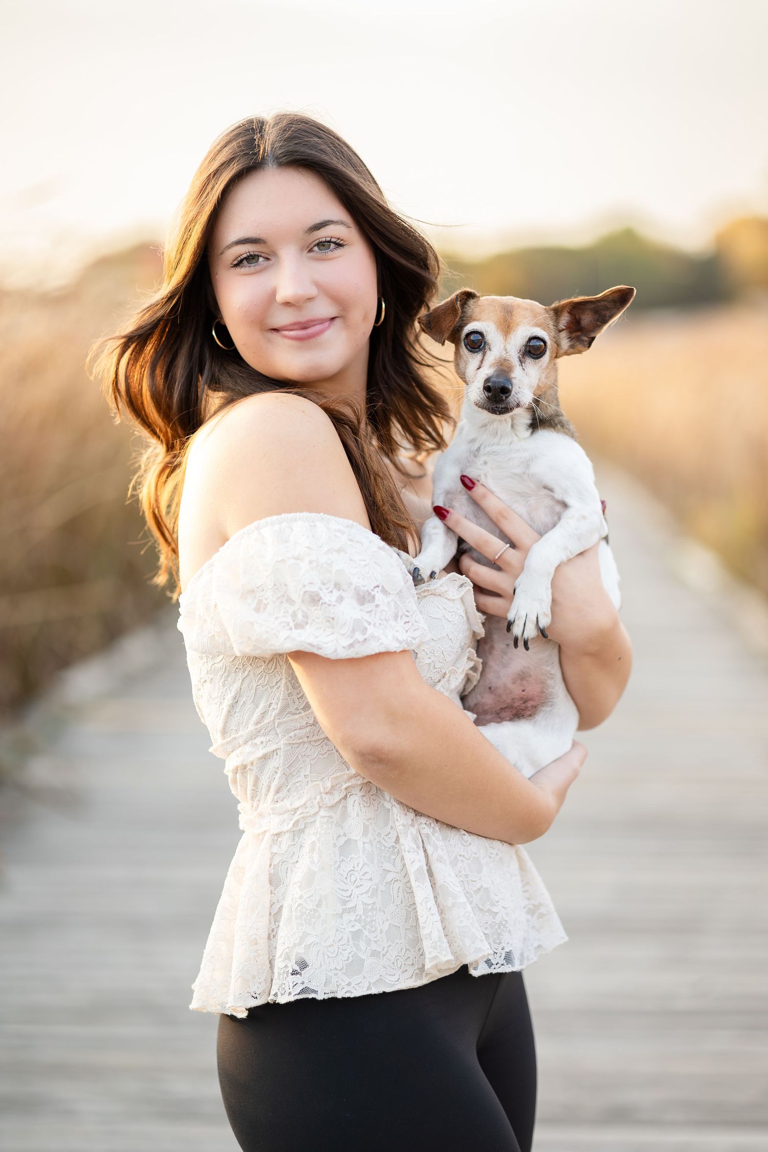 Portrait session with small dog in white lace top and black pants at sunset.