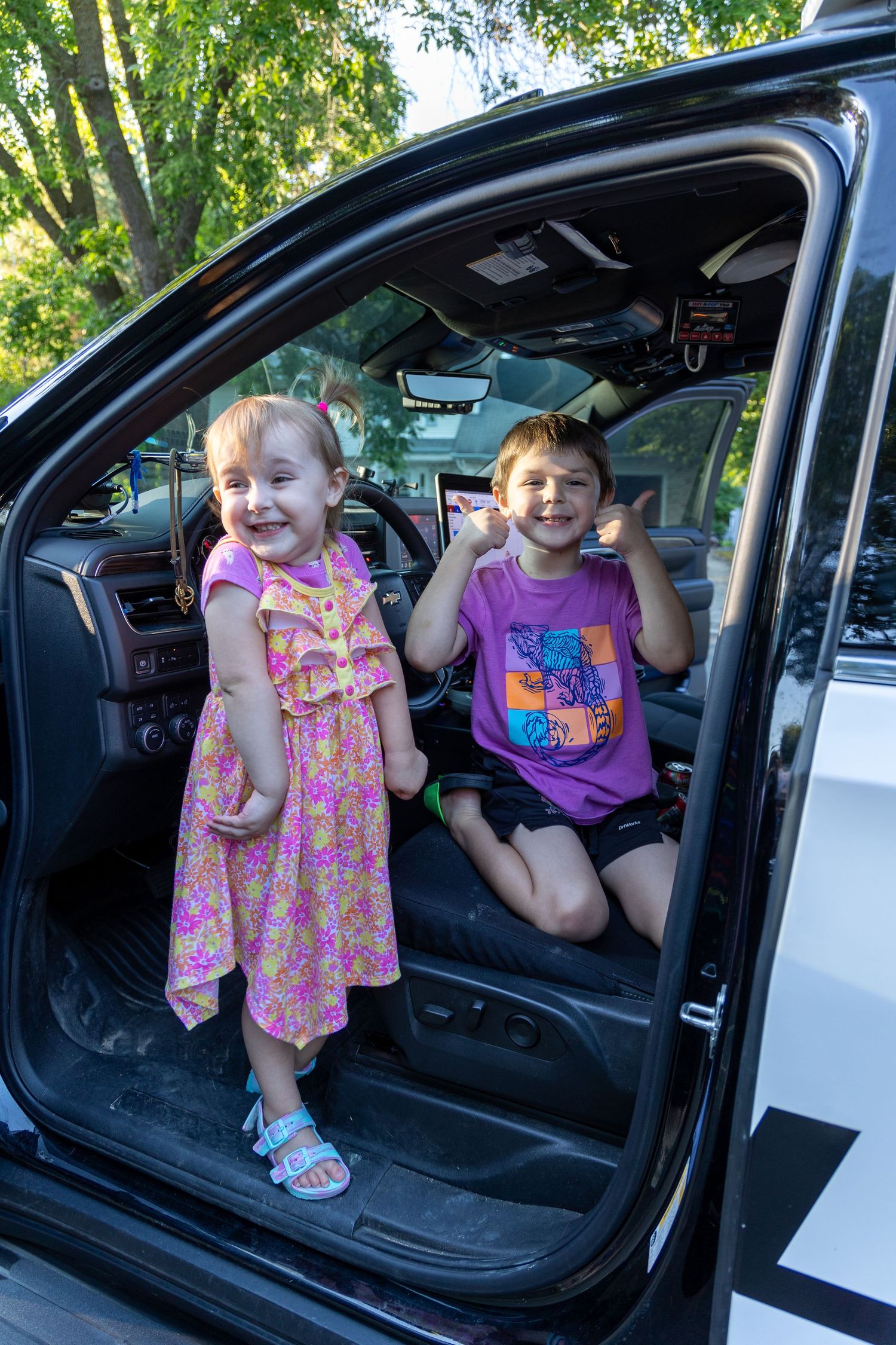 Two children sit excitedly in front seat of police patrol vehicle during community event.