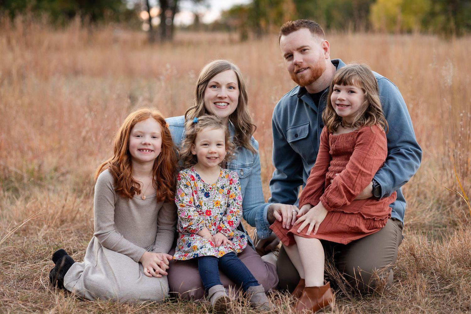 Casual family portrait session in golden autumn field with natural poses.