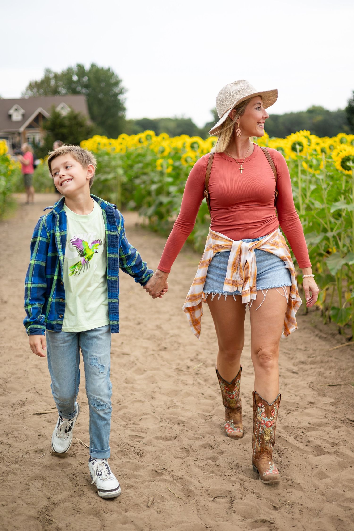 People walk together along a dirt path beside rows of tall sunflowers.