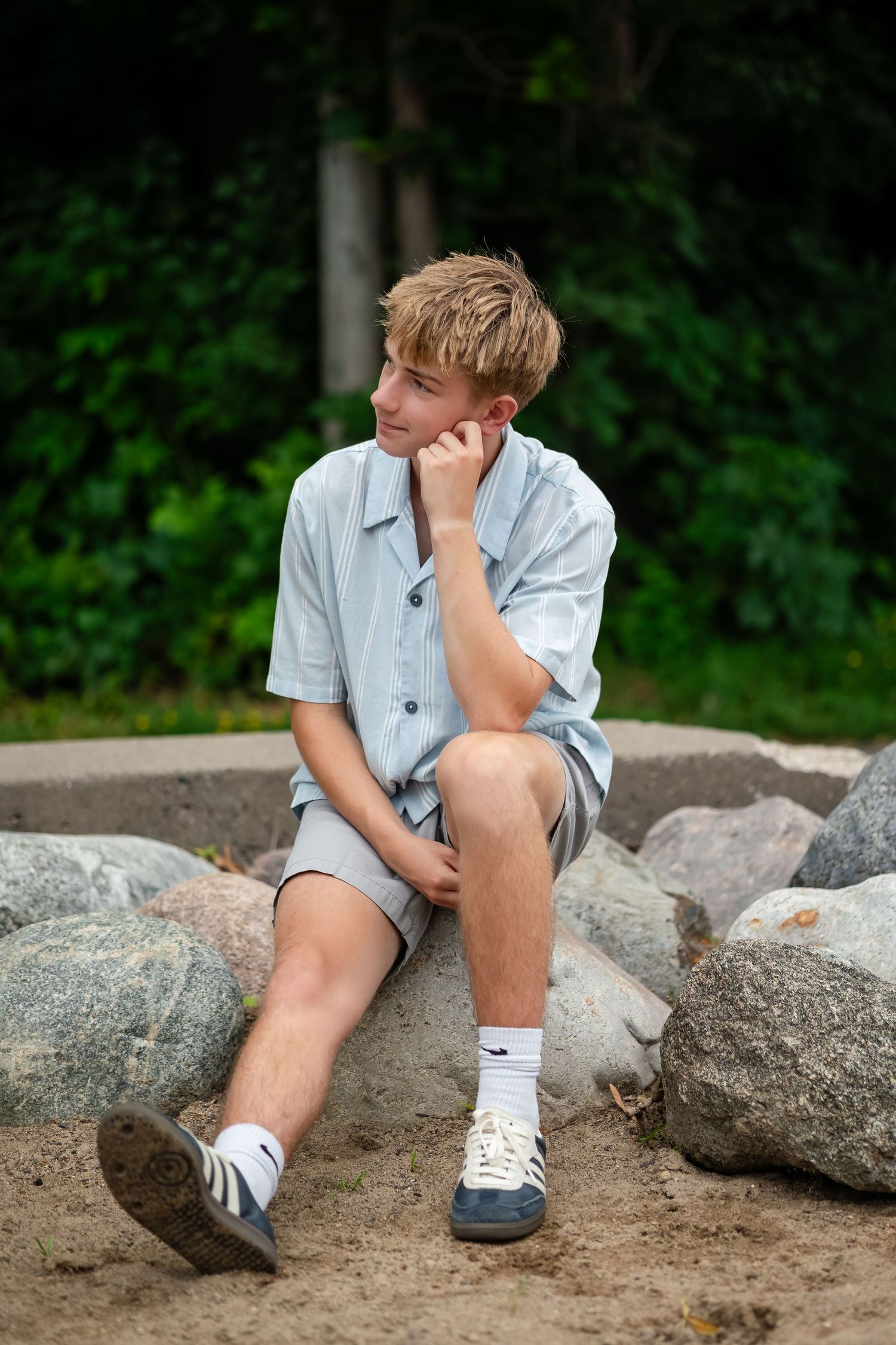 Young boy in casual clothes sitting thoughtfully on large rocks.