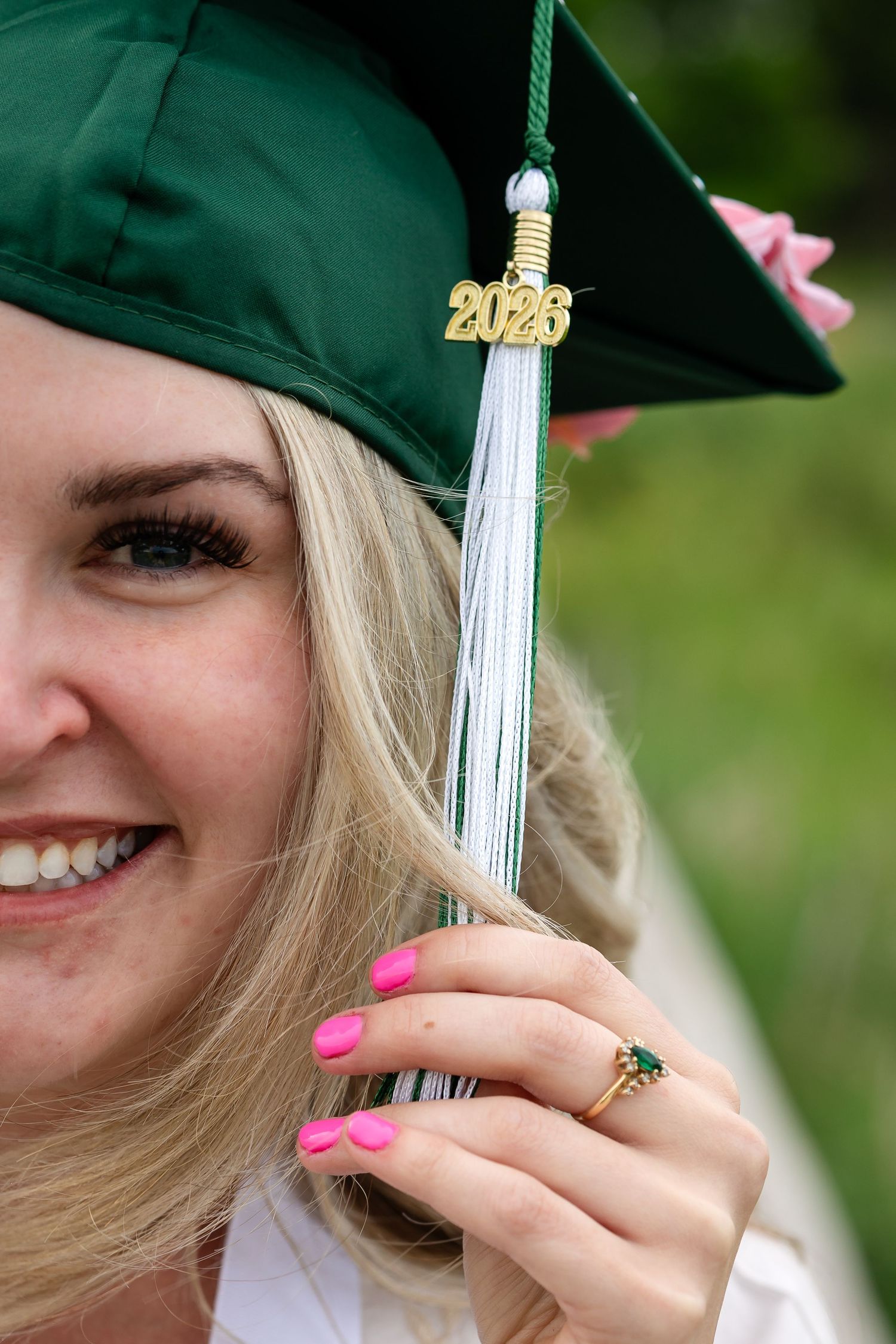 Close-up of a 2026 graduate in green cap holding tassel with pink nails and ring.