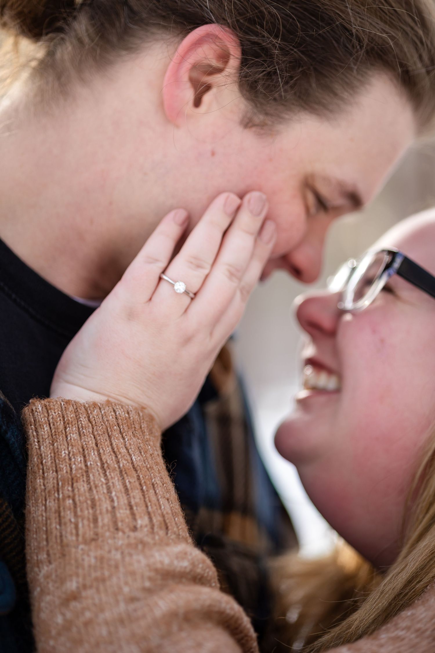 Close-up of smiling couple nearly kissing, woman's hand with engagement ring tenderly touching man's face.