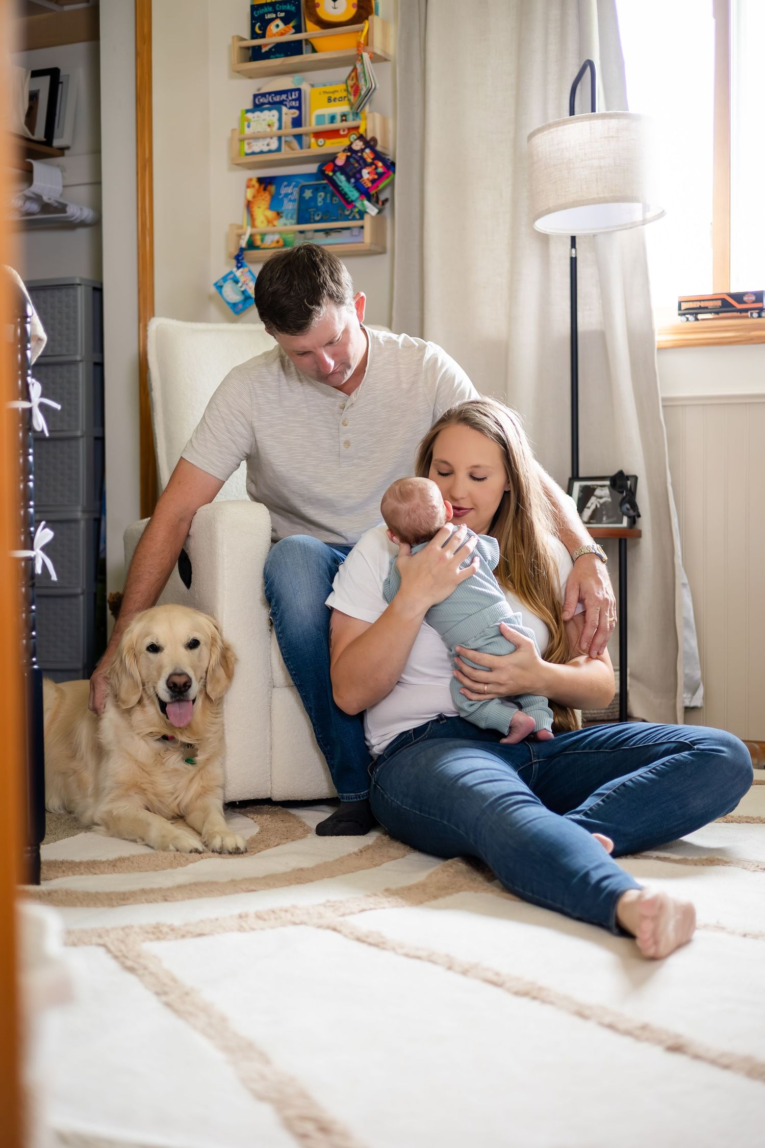 Family relaxing on floor with golden retriever and baby in cozy nursery setting.