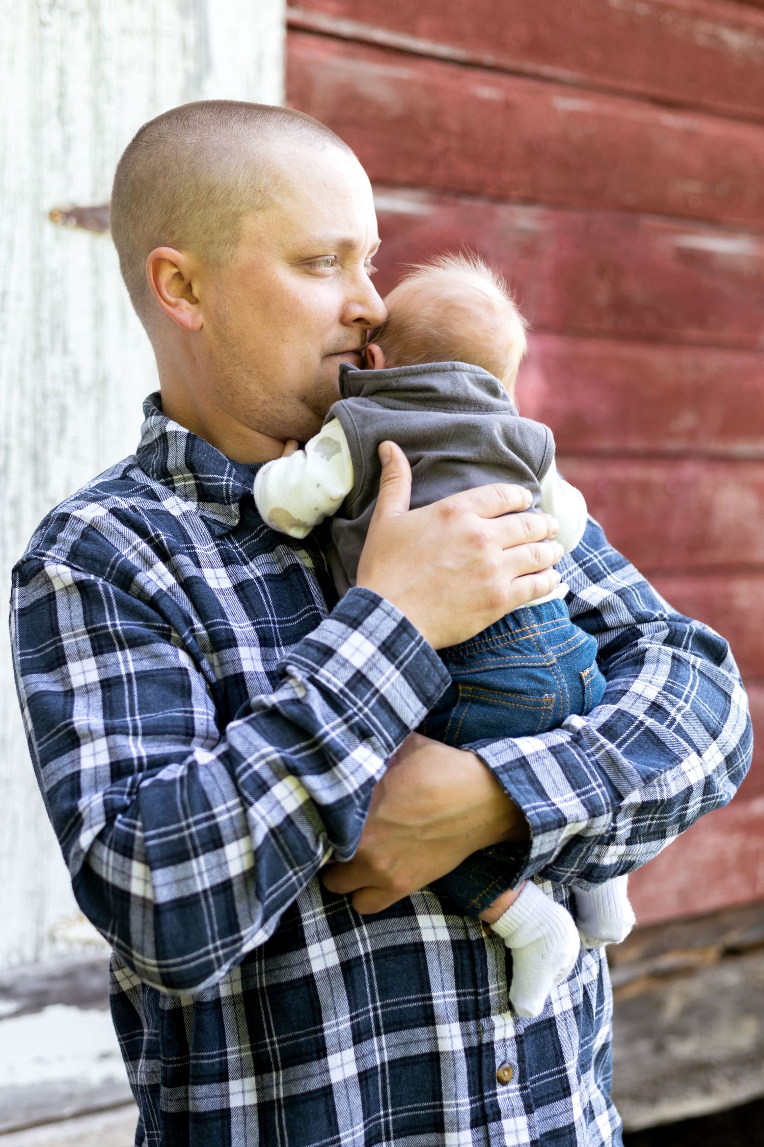 Series of intimate photos showing parent in plaid shirt holding and kissing baby against red barn background.