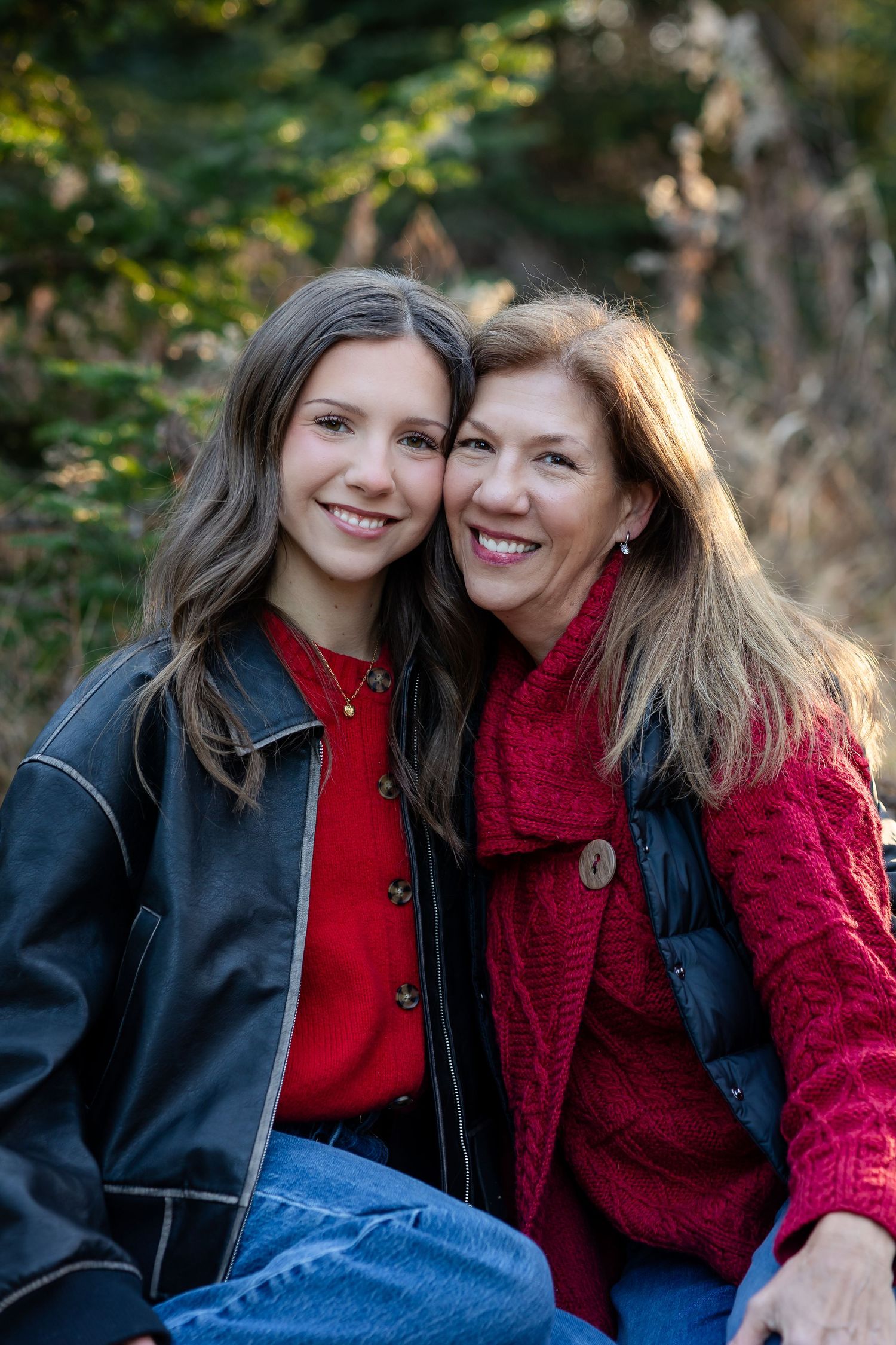 Two people in red sweaters share a close moment outdoors against natural foliage.
