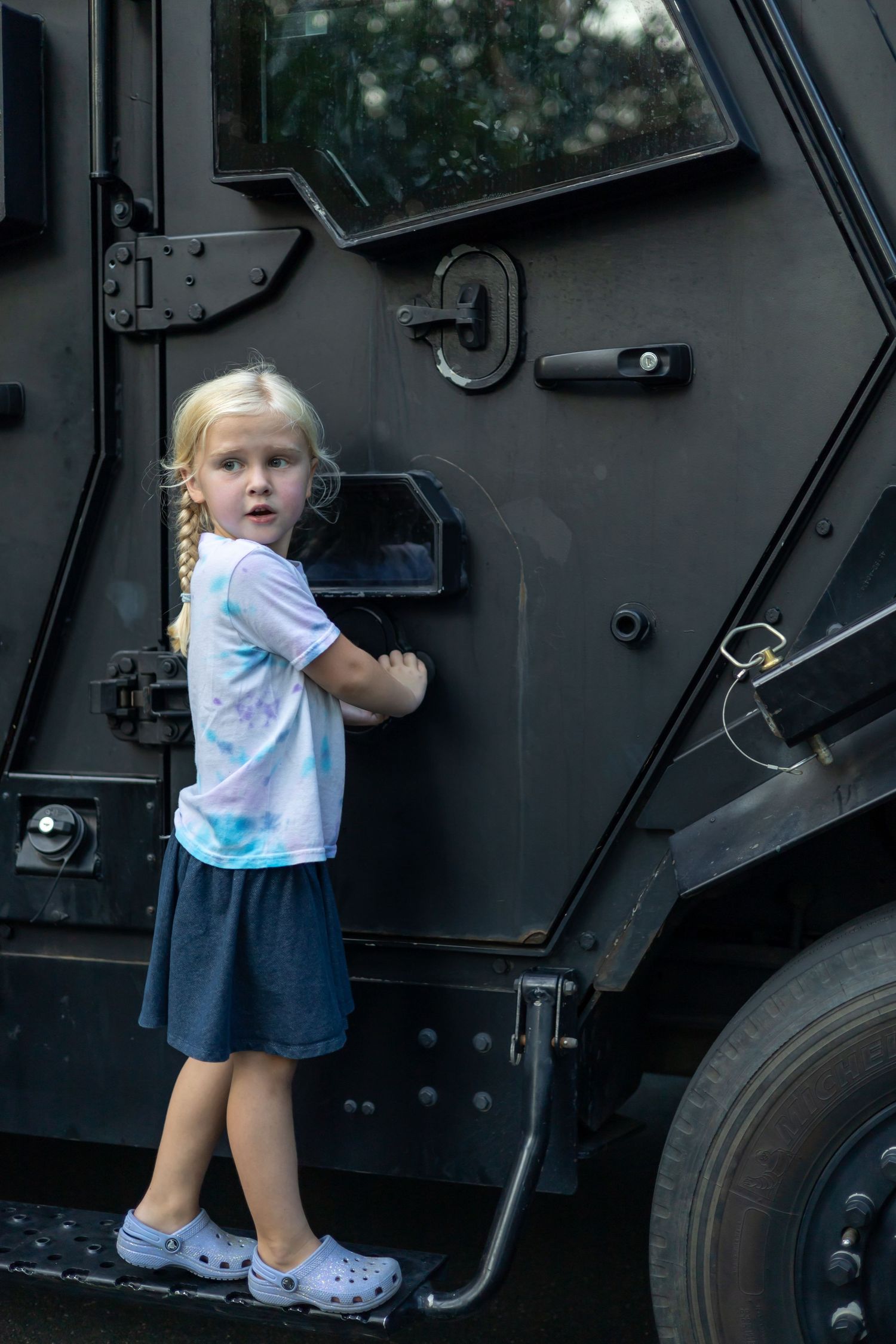 Child exploring and climbing on a large black armored vehicle.