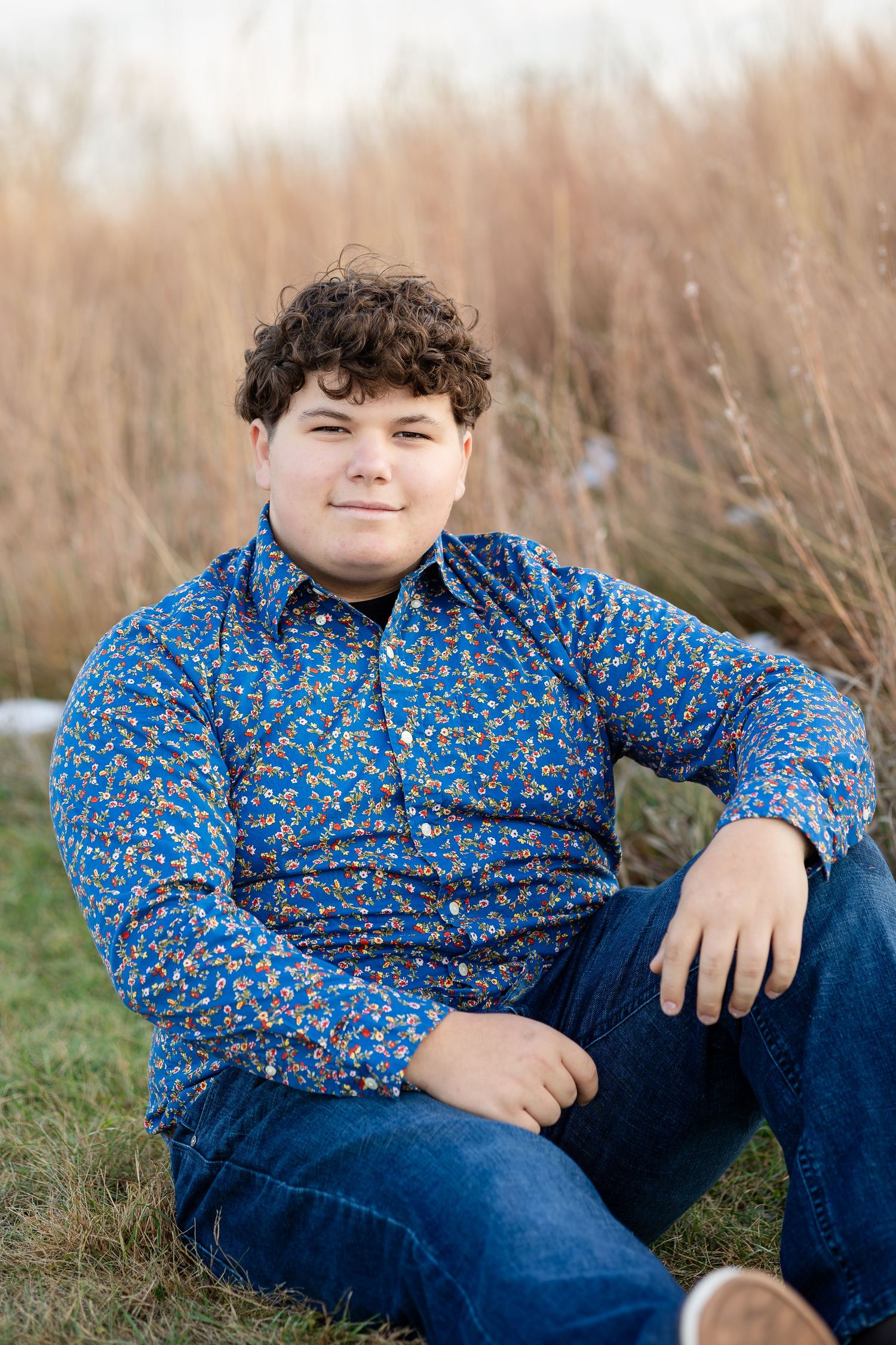 Person in blue floral shirt reclining in tall autumn grass during golden hour.