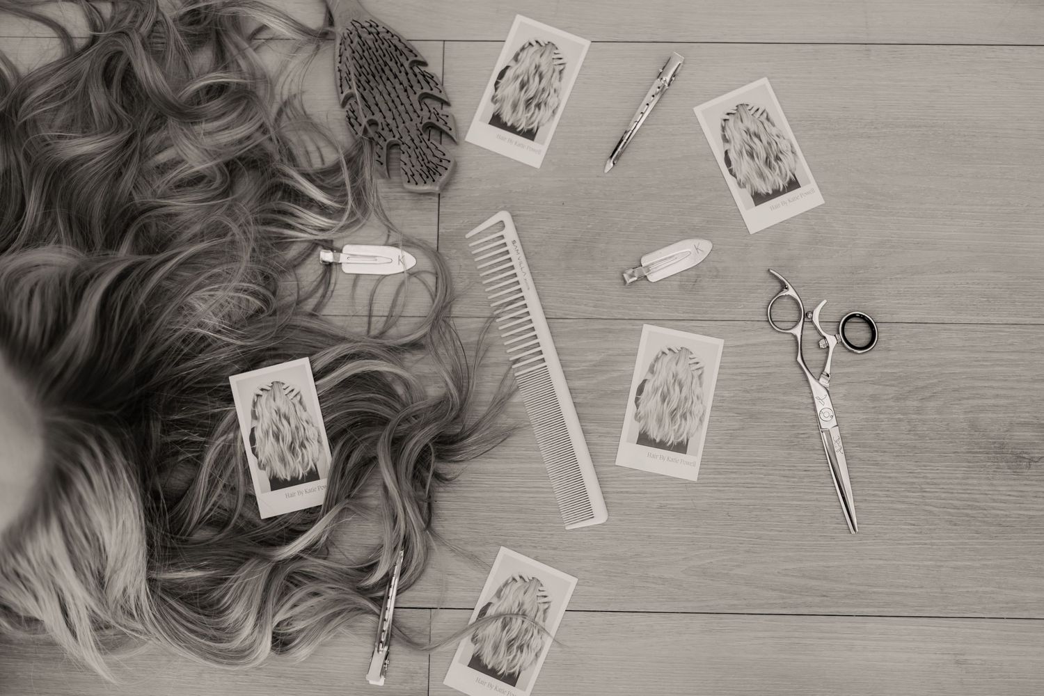 Hair extensions and styling tools arranged on a light gray wooden surface with scattered photographs.