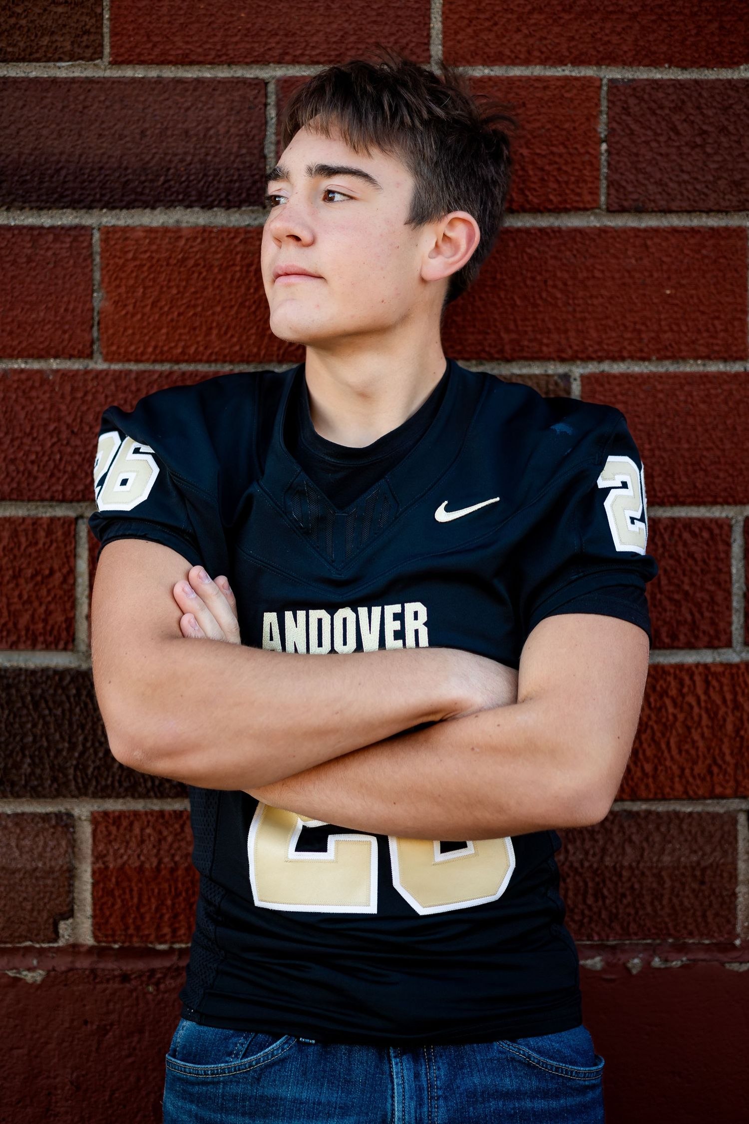 Athletic figure in black Andover football jersey number 26 poses with arms crossed against brick wall.