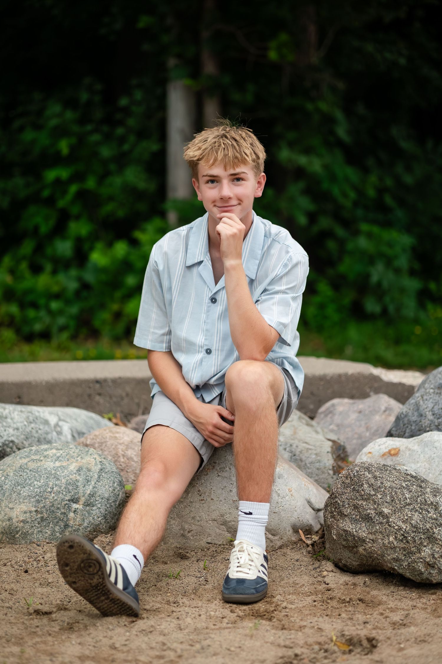 Person in casual summer attire sits thoughtfully on large rocks outdoors.