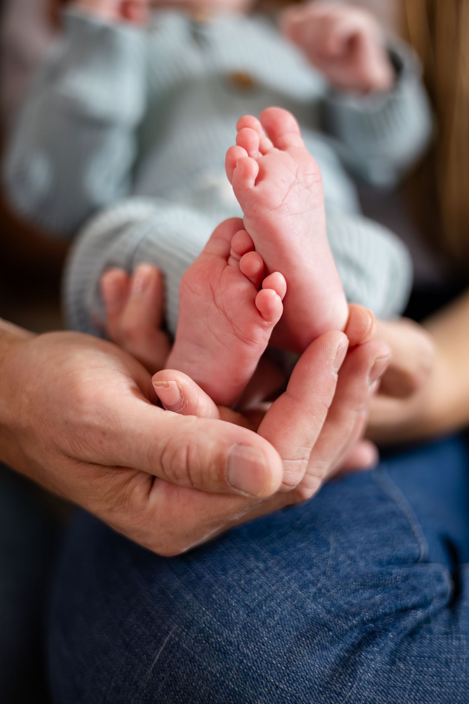 Close-up series of tiny baby feet being gently held in adult hands on denim background.