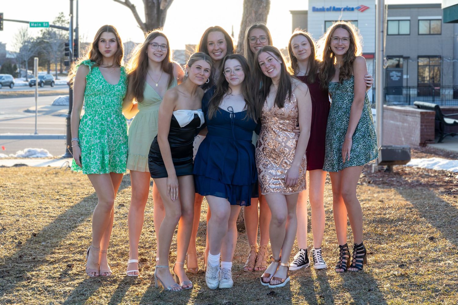 Group of friends in colorful dresses and outfits standing together outdoors at sunset.