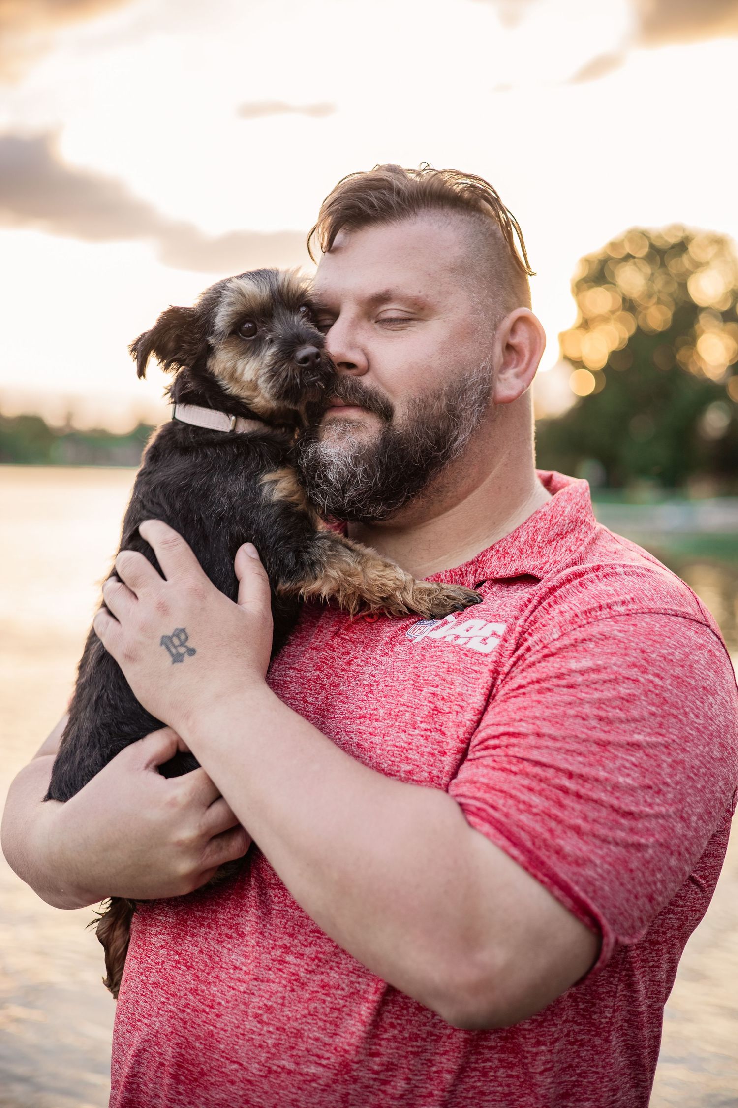 A small dark terrier being held and cuddled at sunset.