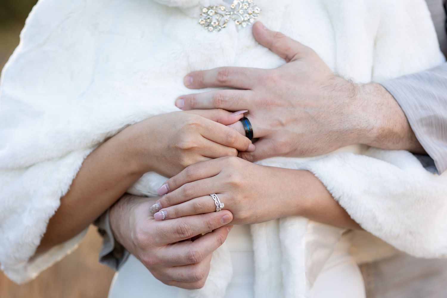 Close-up of hands showing wedding rings against white fabric.