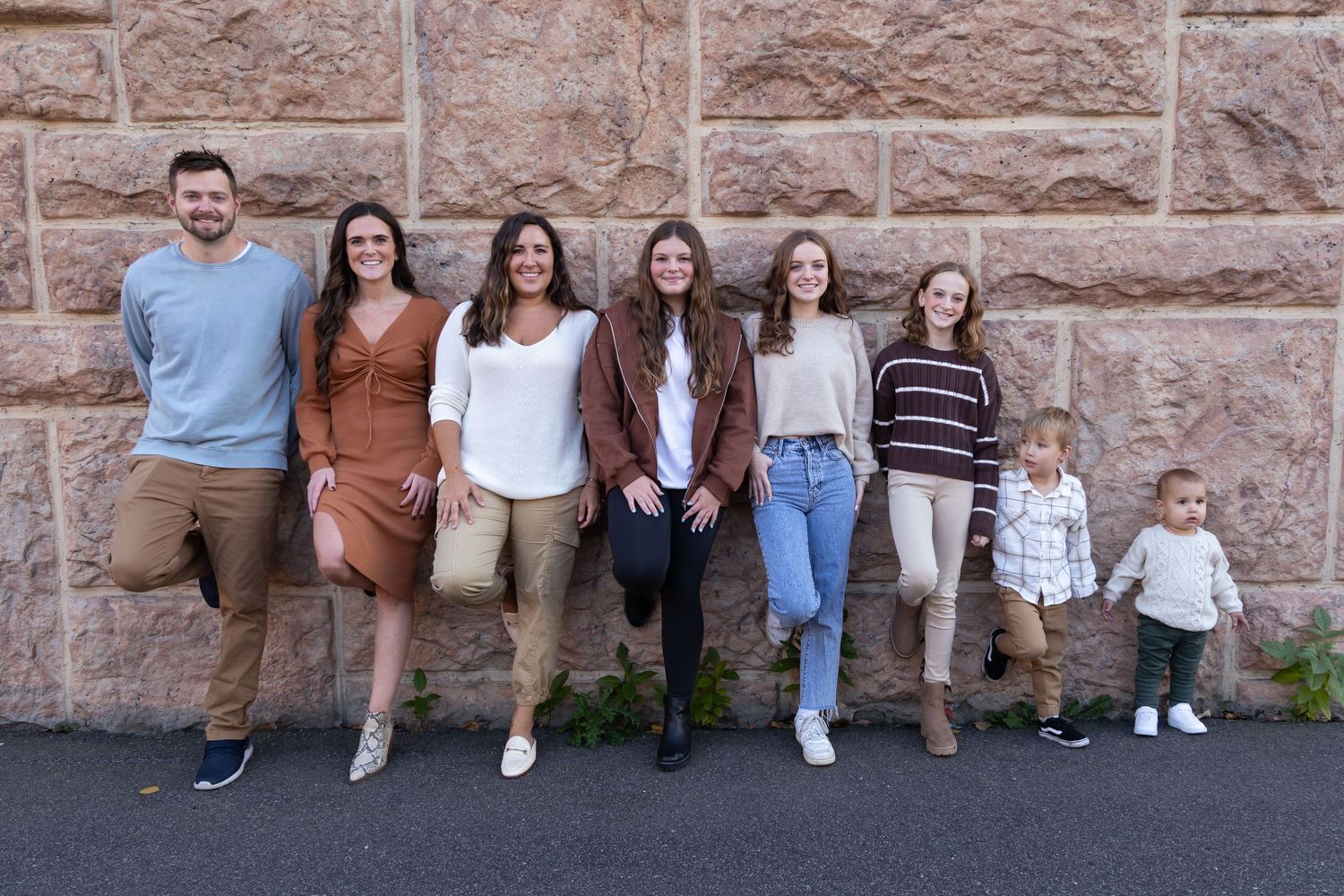 A group of people posing casually against a textured stone wall background.