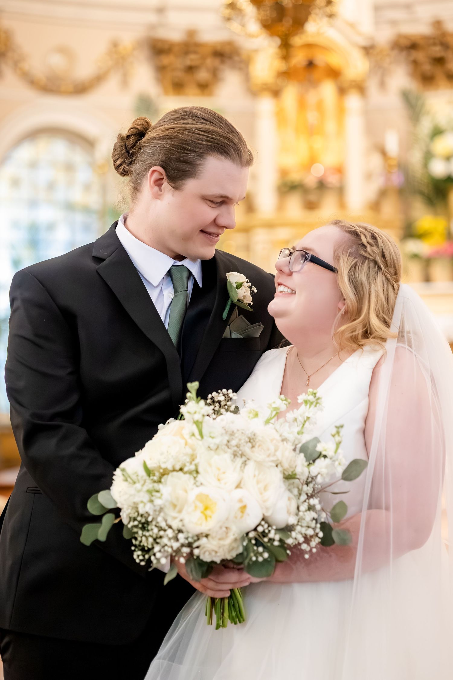 Smiling bride and groom holding white floral bouquet inside ornate church interior.