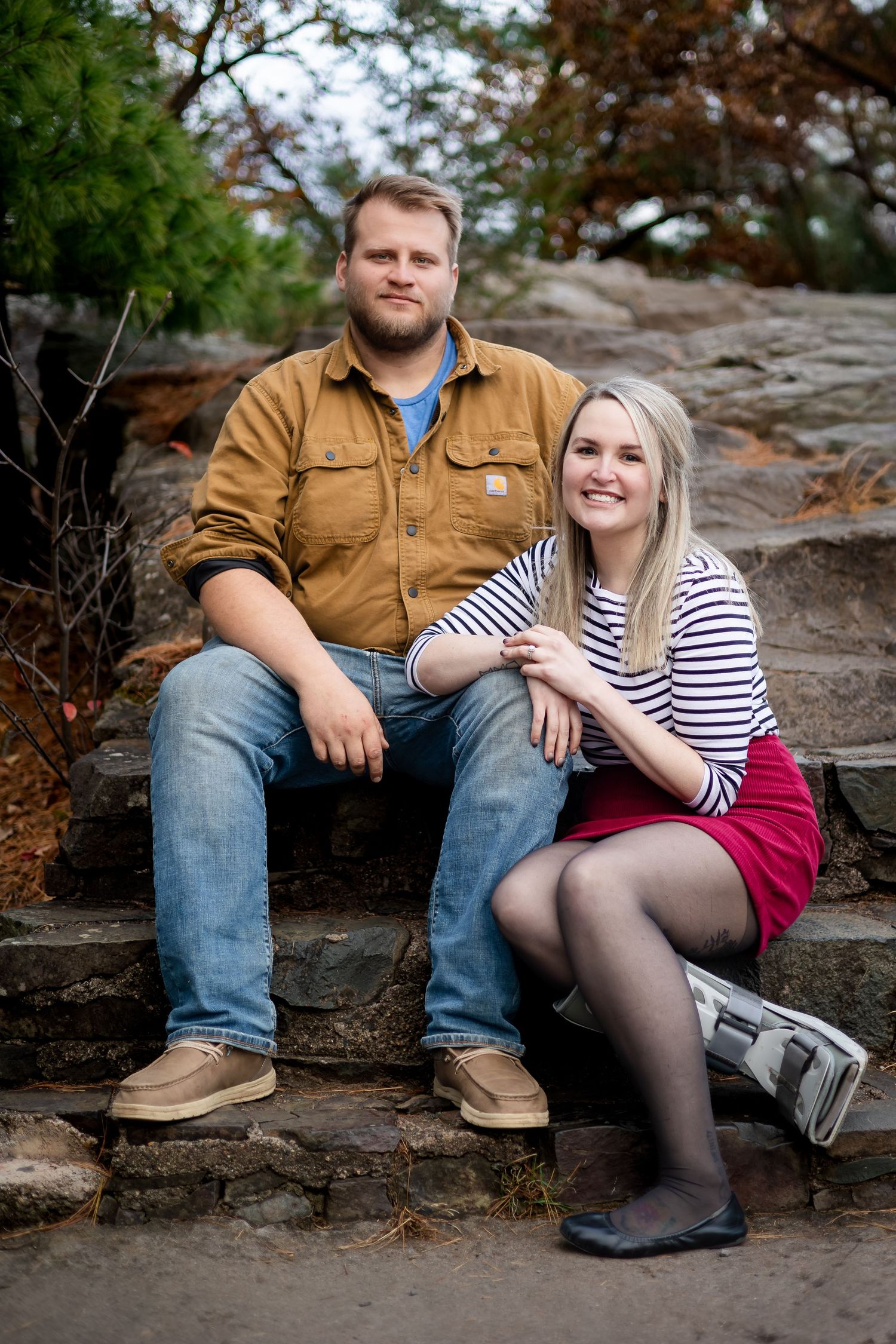 Couple sitting on stone steps outdoors, woman in striped shirt and red skirt smiling.