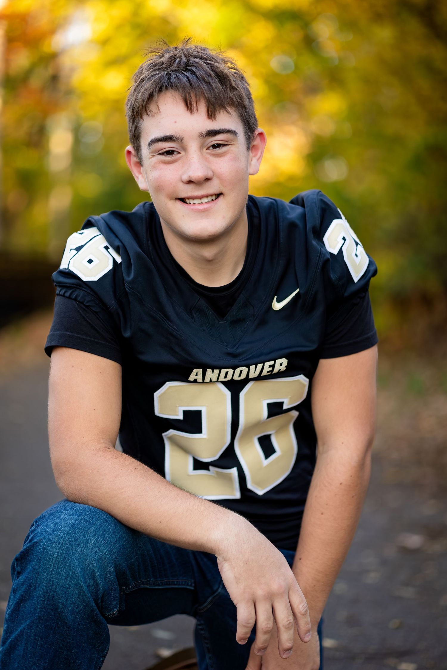 High school football player wearing Andover jersey number 26 poses for portrait with autumn foliage in background.