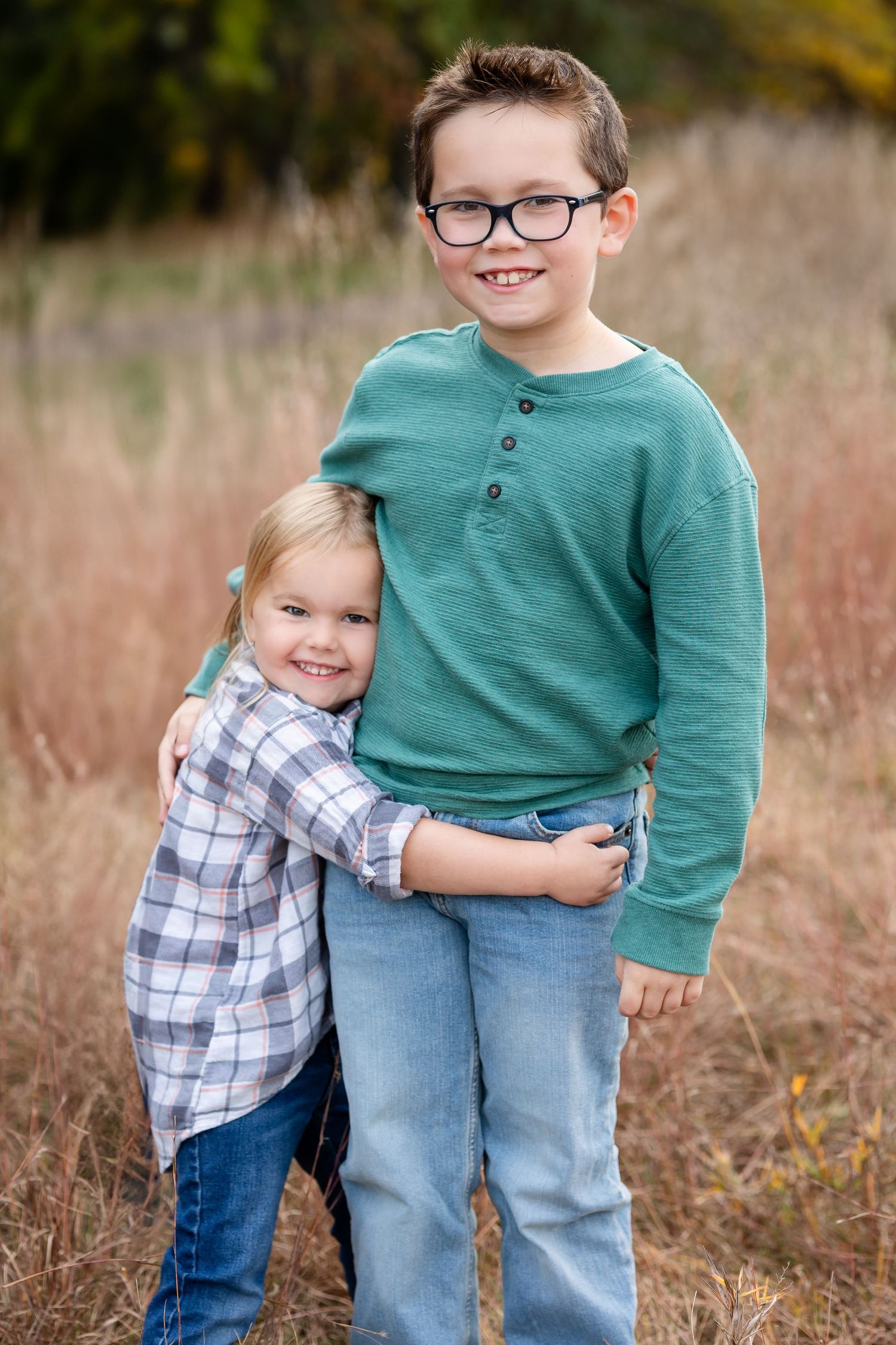 Siblings sharing a warm embrace while standing in tall autumn grass.