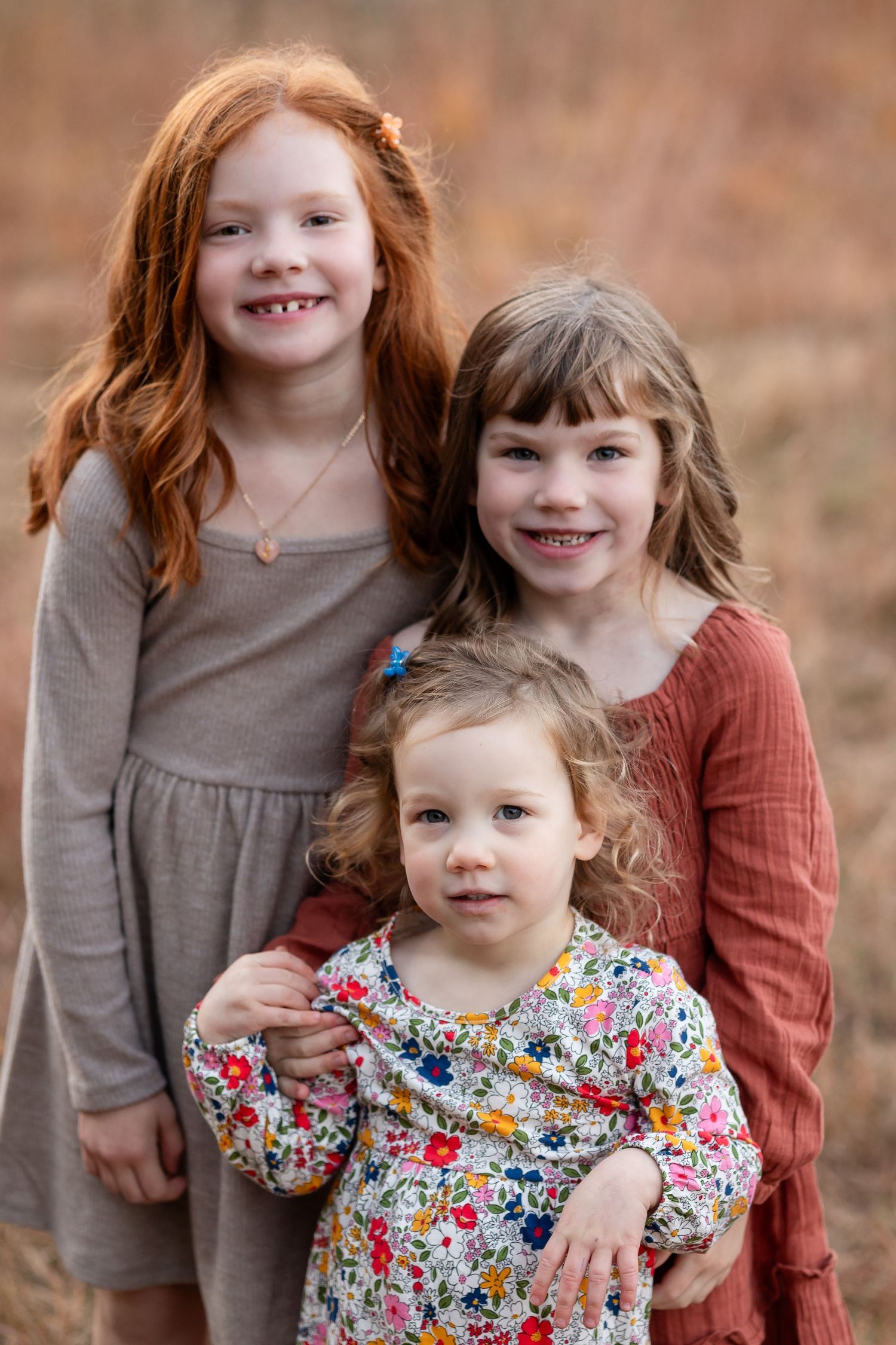 Sisters in coordinated dresses posing together in autumn field.
