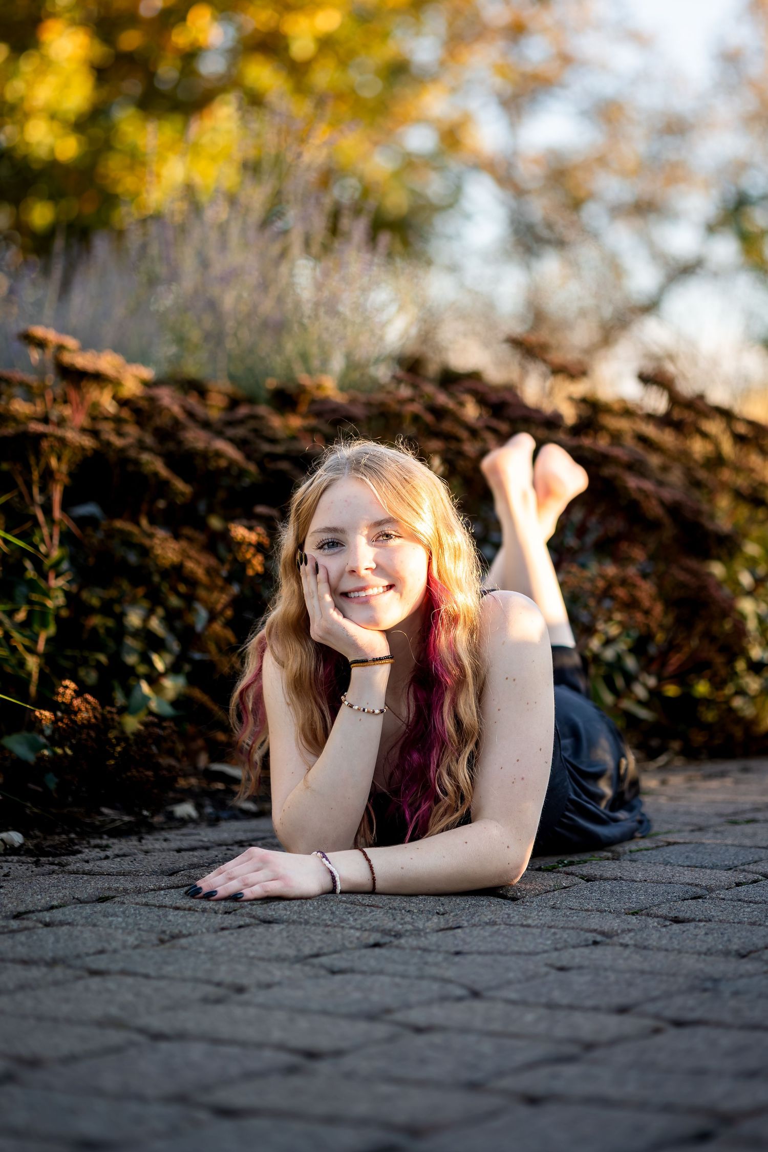 Person with two-toned hair lying on ground with autumn foliage and golden bokeh in background.