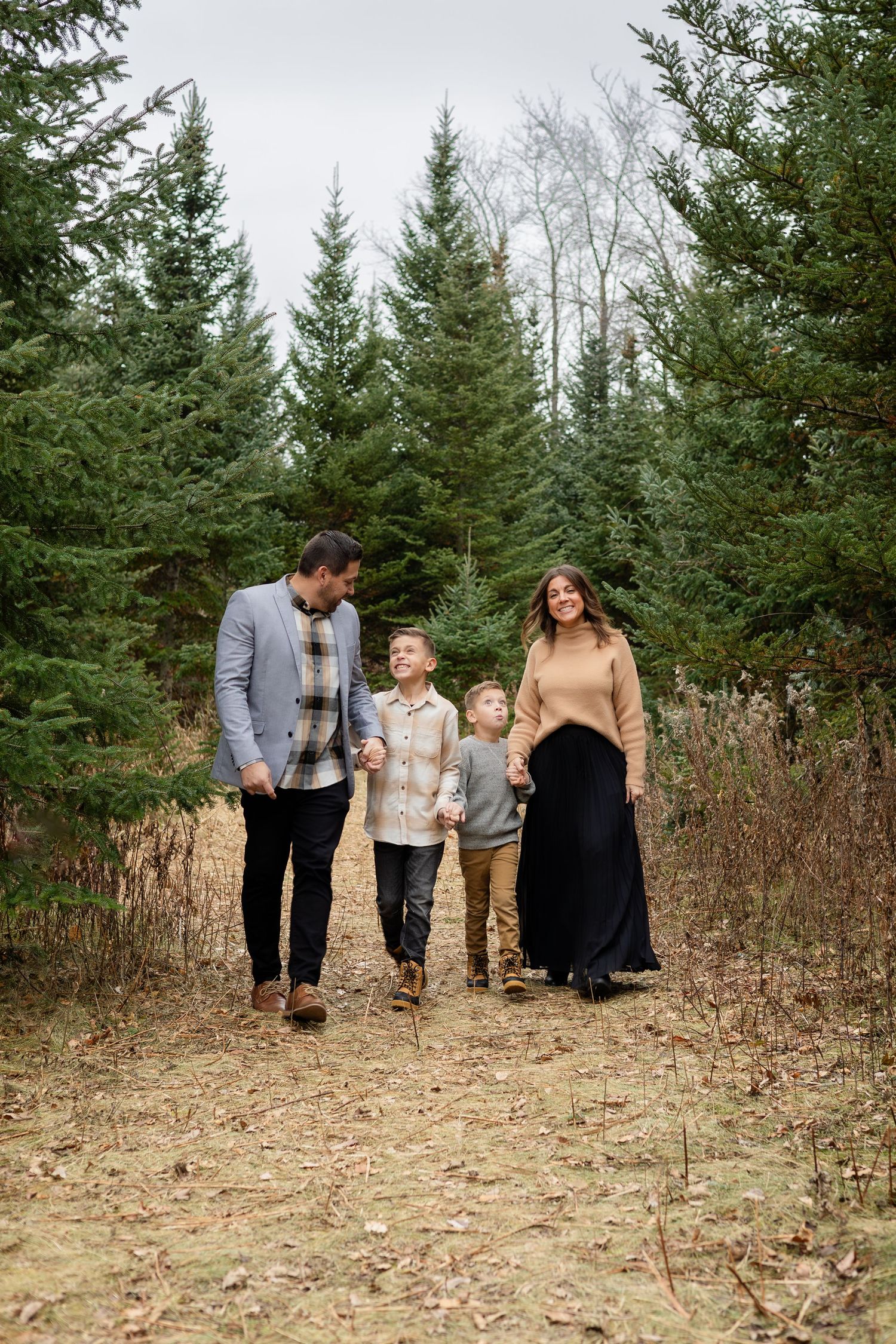 A family walks together through a clearing surrounded by tall evergreen trees.