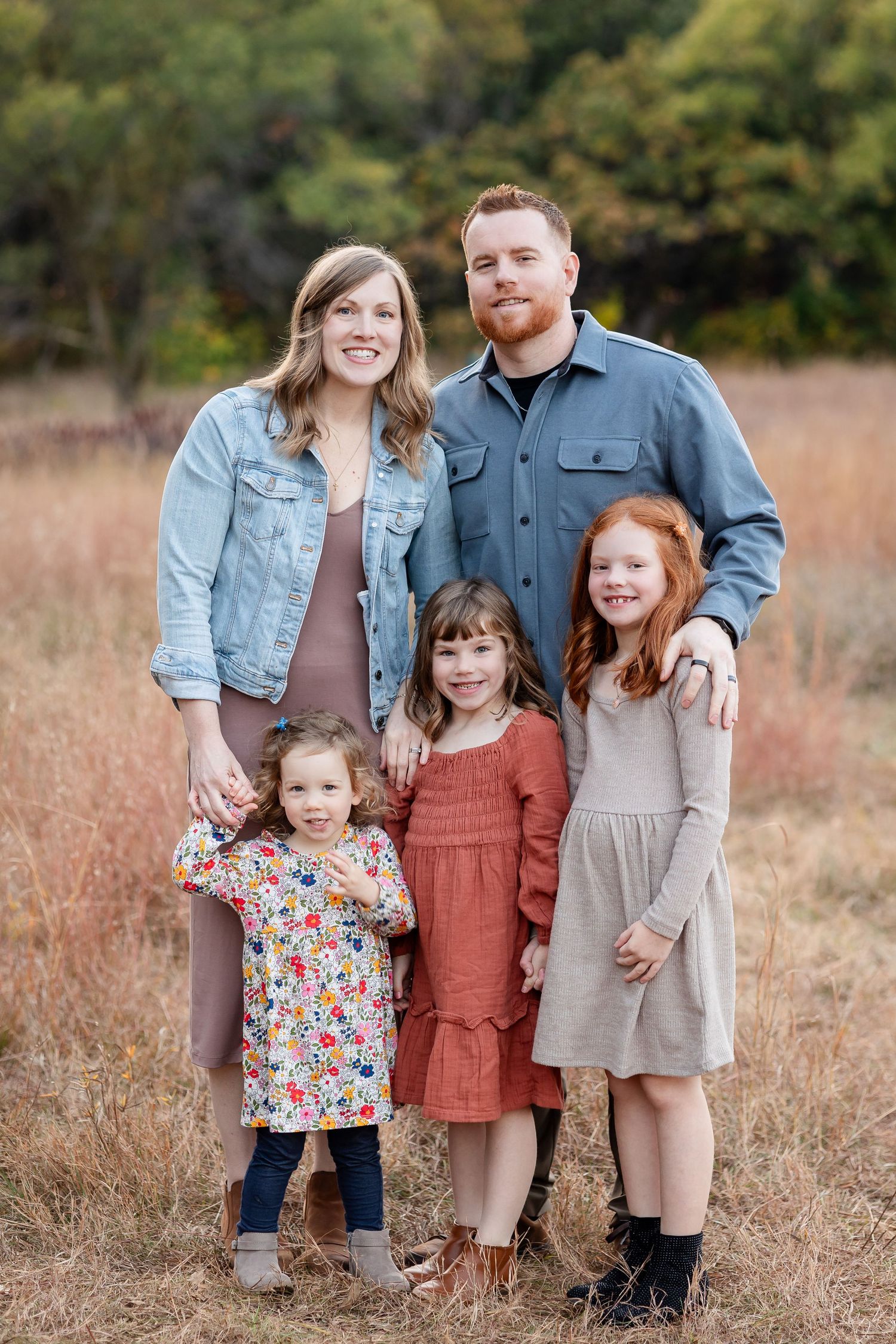 Family portrait in casual coordinated outfits standing in autumn field.