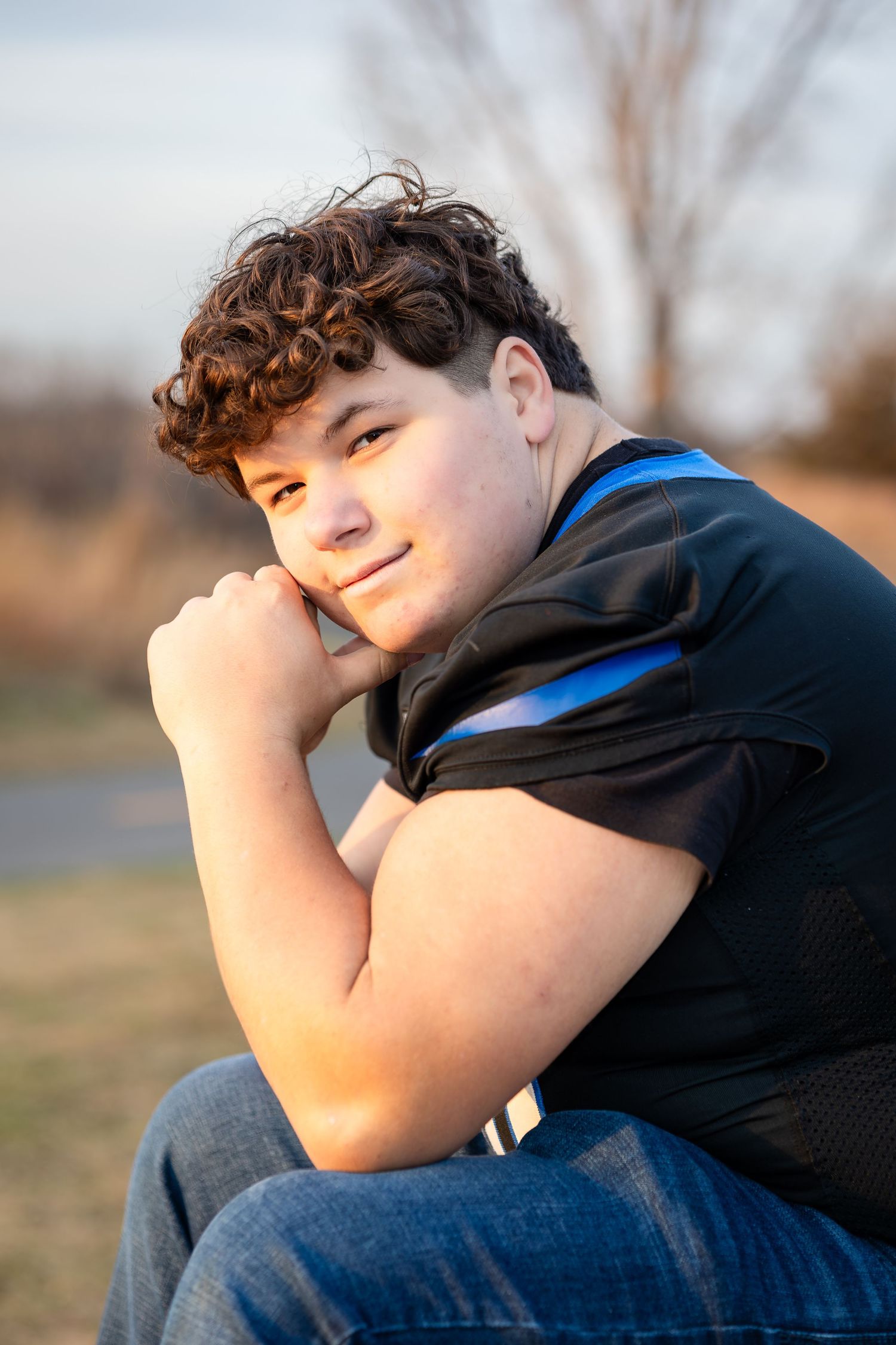 Person in black shirt reclines thoughtfully against outdoor setting in warm light.