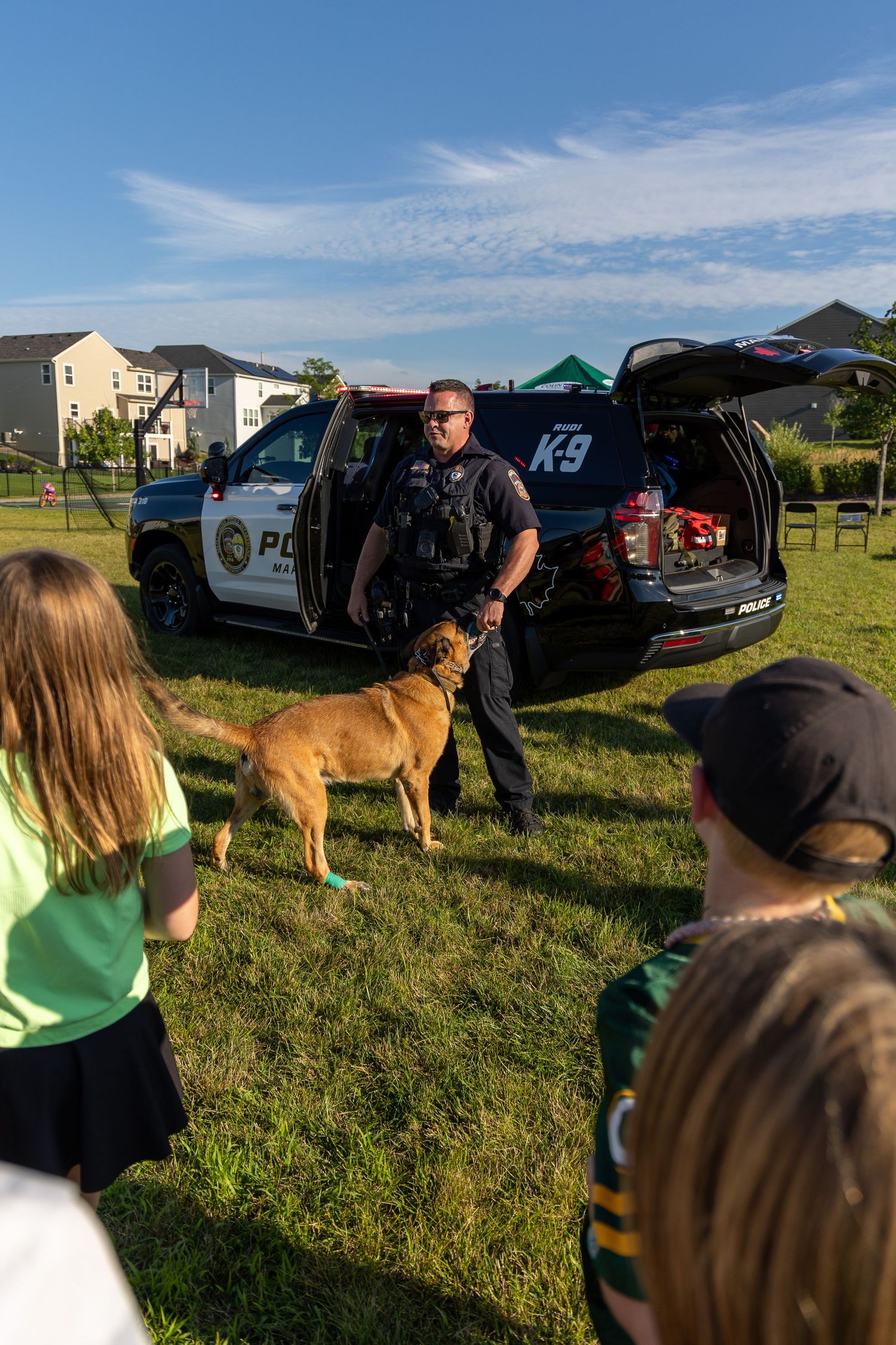 Police K-9 unit demonstrates with service dog in front of patrol vehicle at community event.