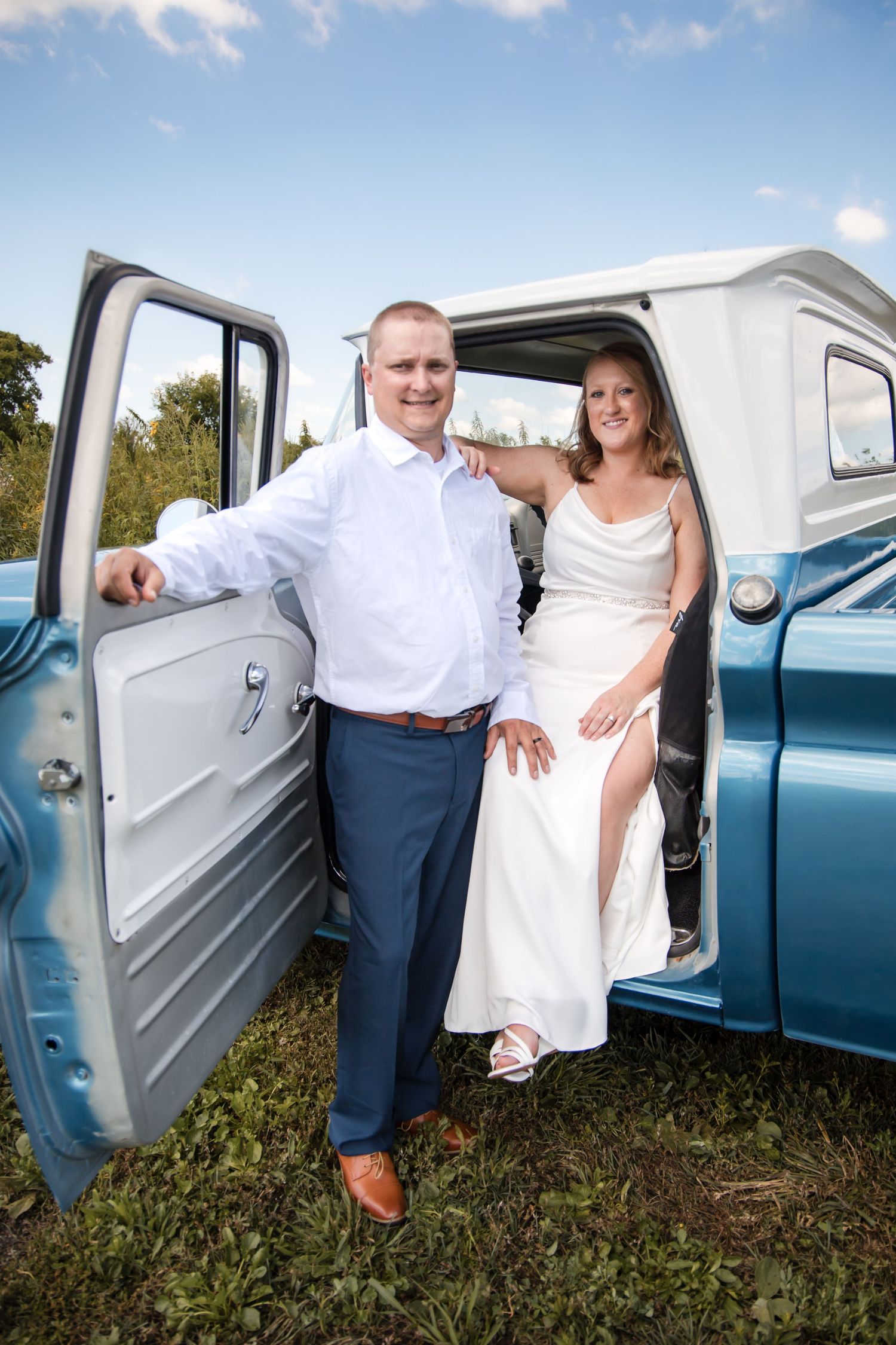 Wedding couple posing with a classic blue pickup truck in a rustic outdoor setting.