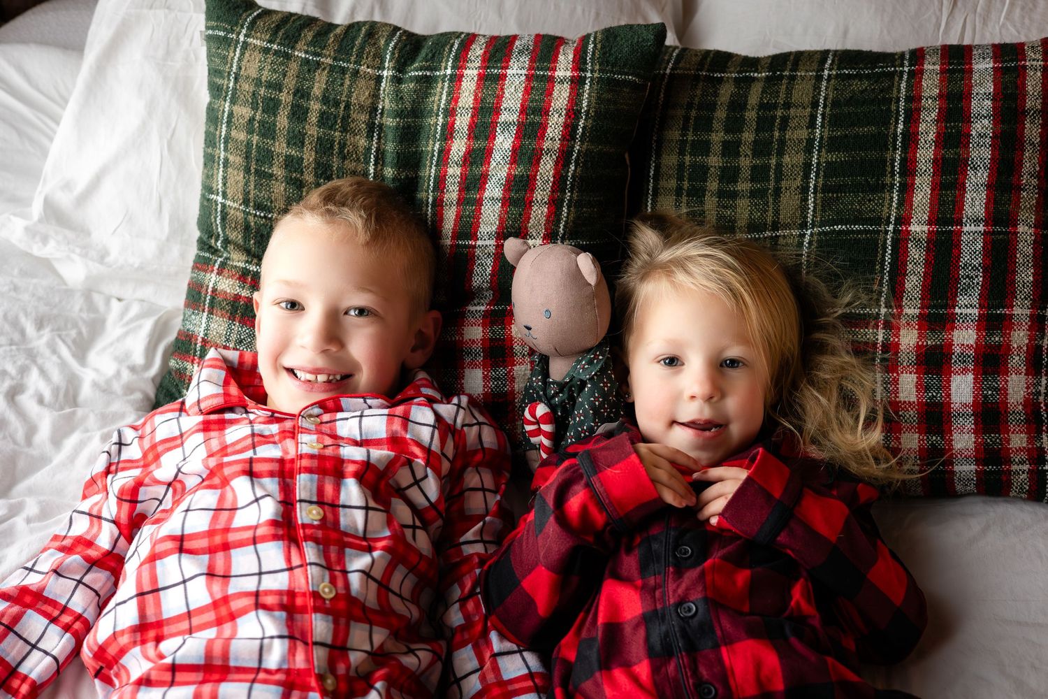 Children in plaid holiday pajamas playing on plaid-patterned couch.