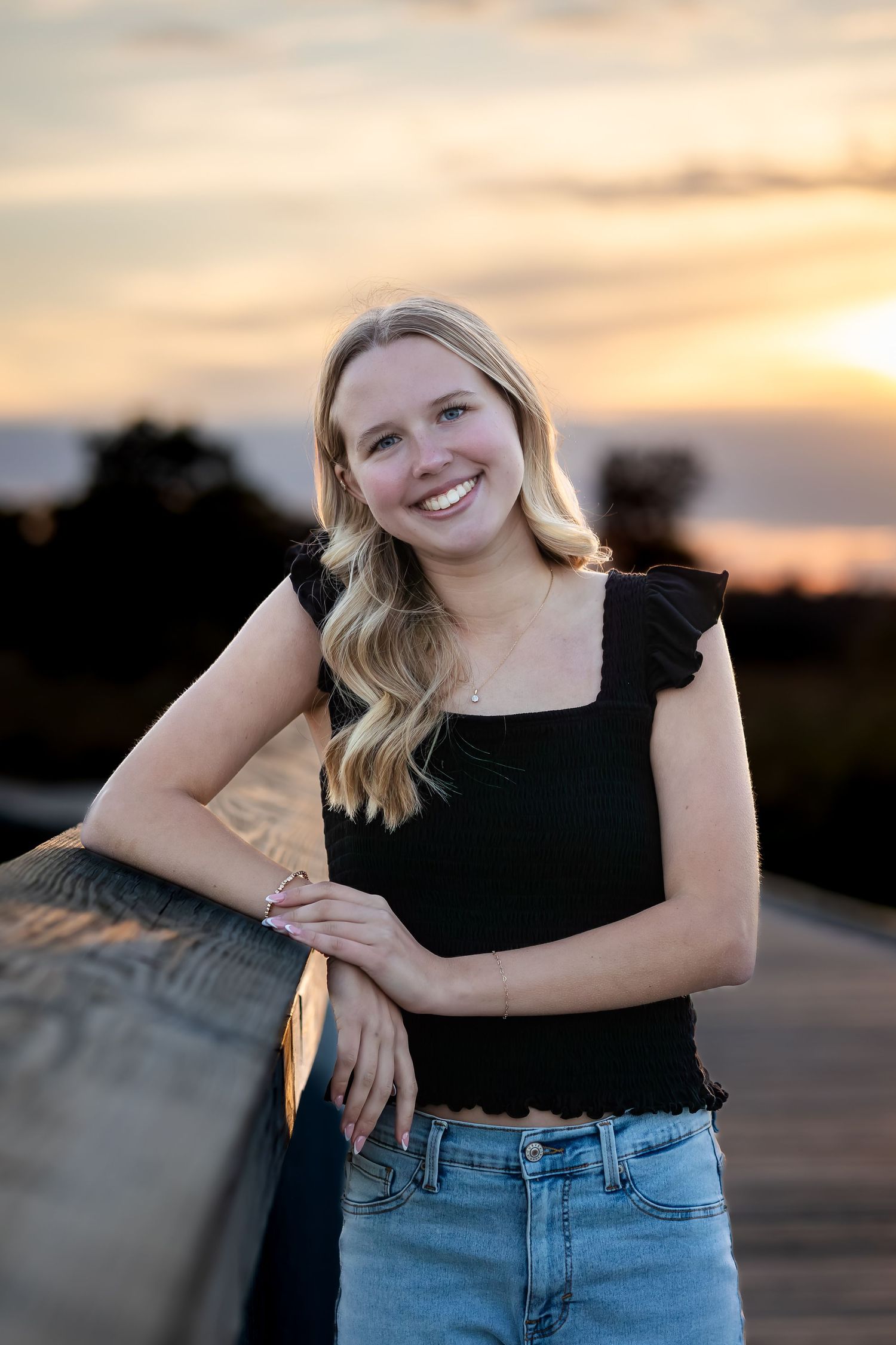 Casual outdoor portraits in black top and jeans during sunset with warm sky backdrop.