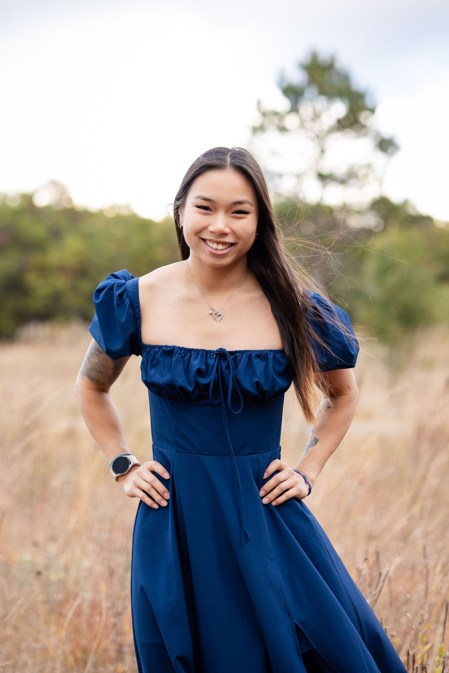 Woman in elegant navy dress poses gracefully in golden field at sunset.