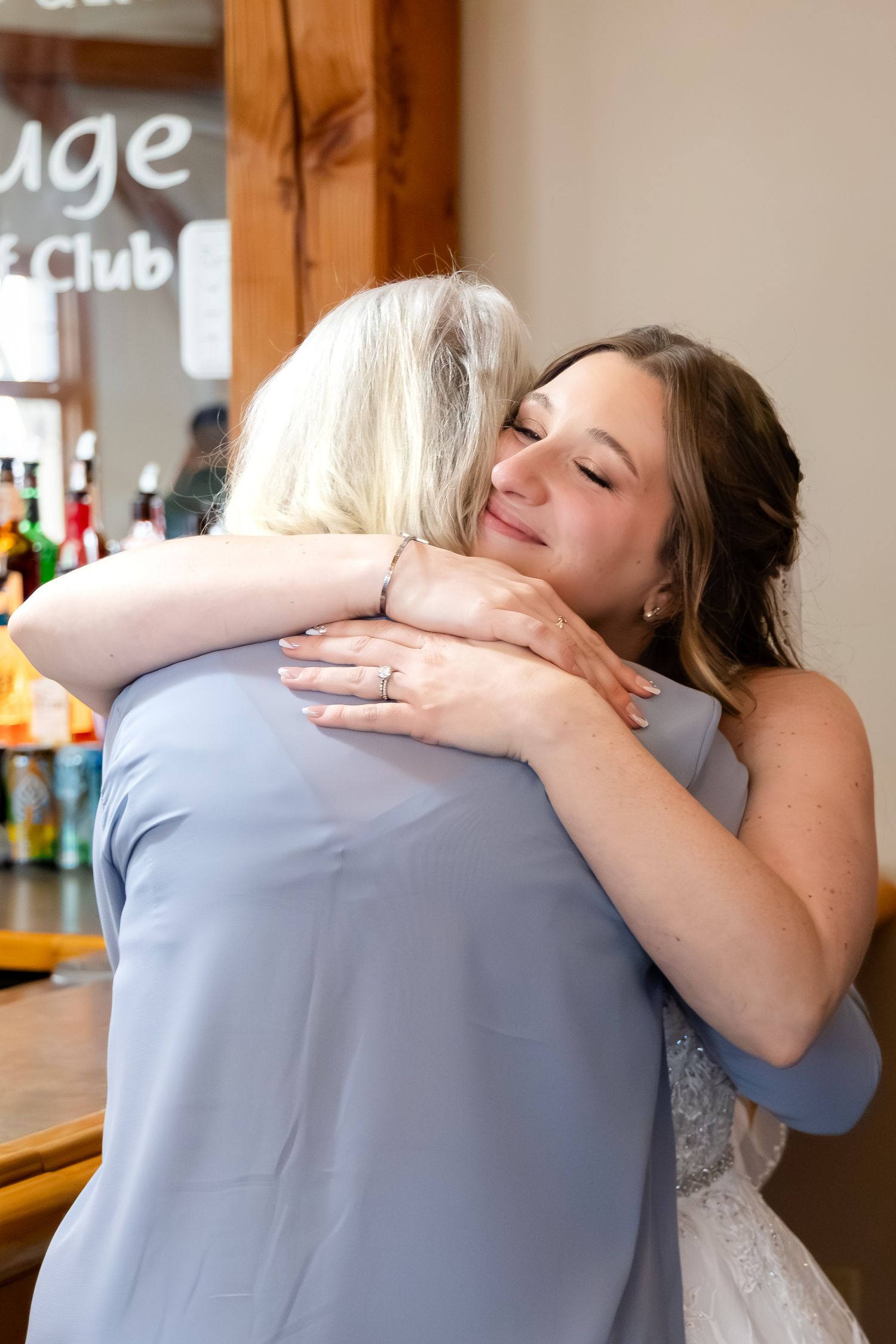 Emotional bride hugs an older woman in a blue dress at the wedding reception.