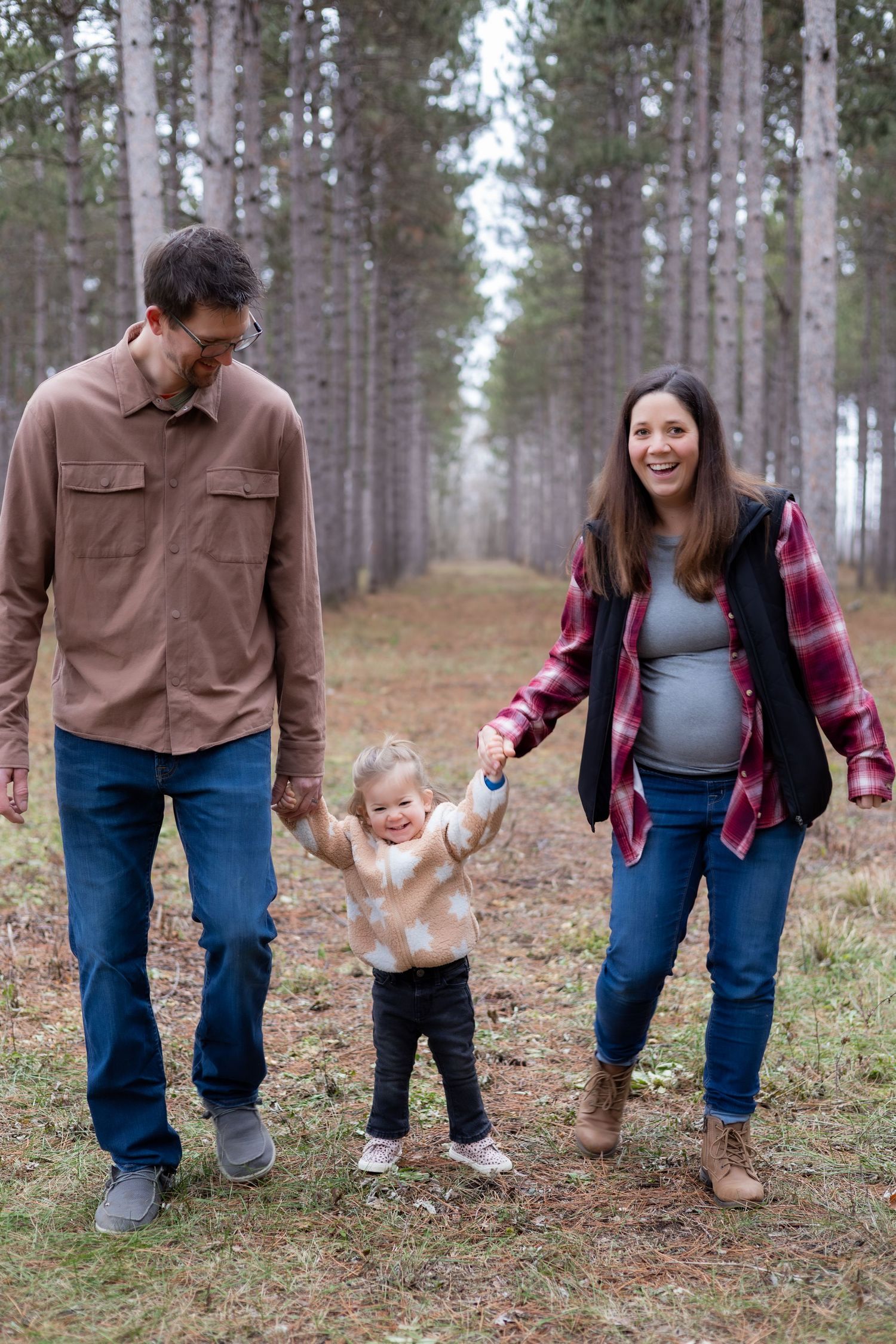 A family walks together holding hands through a pine forest trail.