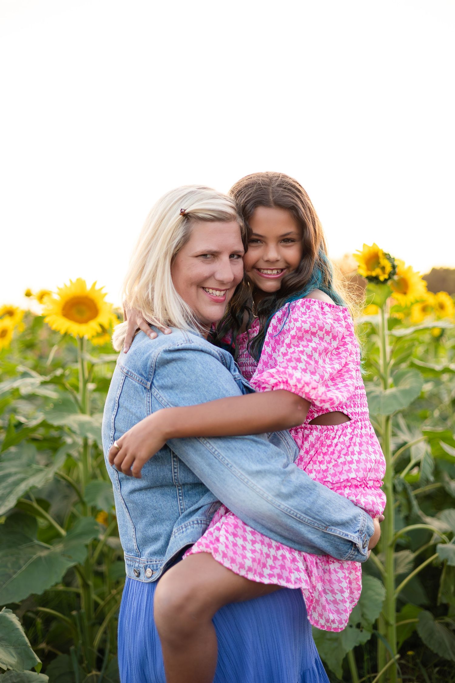 Two people embrace warmly in a field of tall sunflowers during sunset.